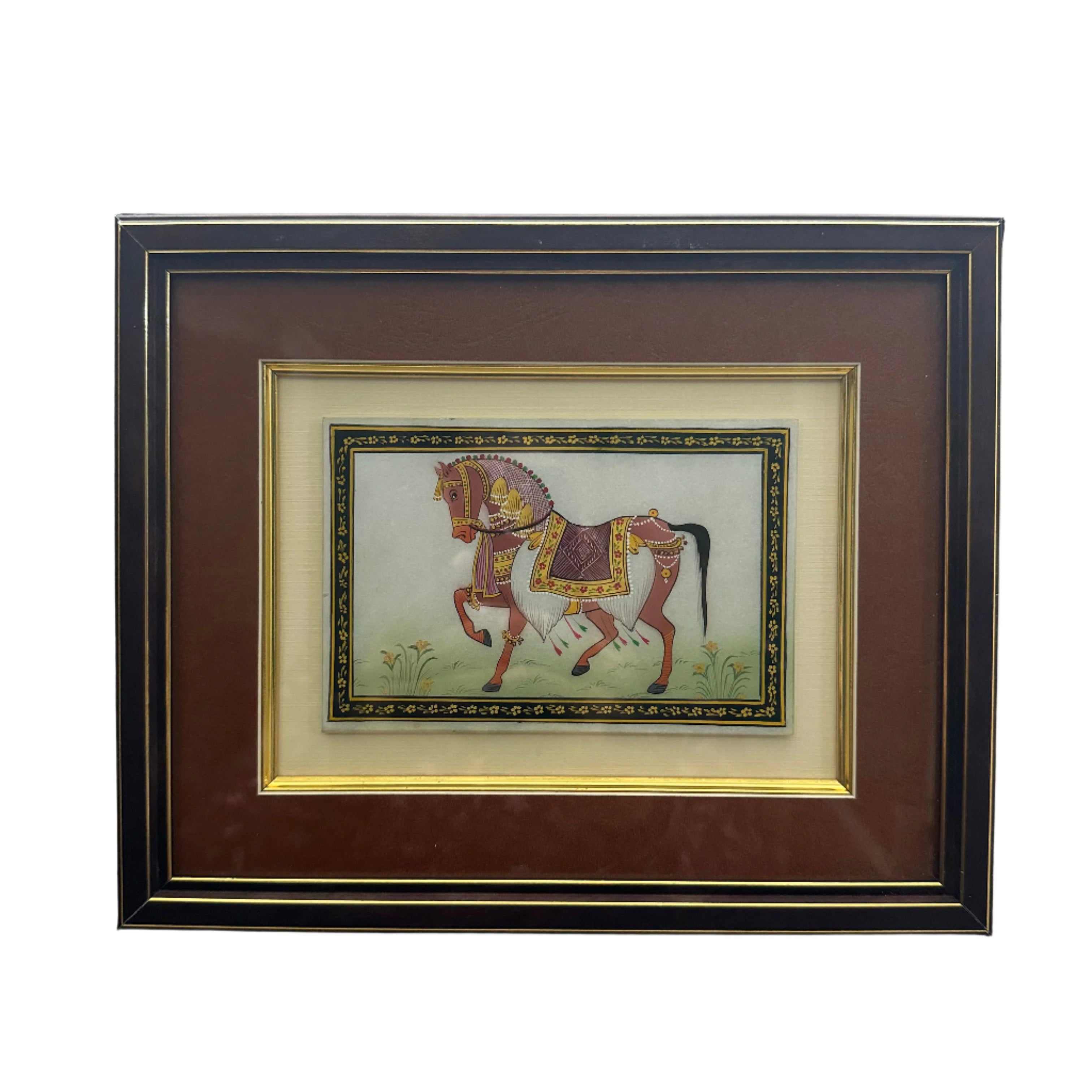 A framed artwork depicting a traditional ornament, with a horse and rider figure, in a wooden frame on a wall.