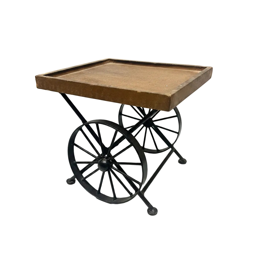 A vintage-style side table with a rectangular brown wooden top and a black metal frame supported by two large spoked wheels, photographed against a white studio backdrop.
