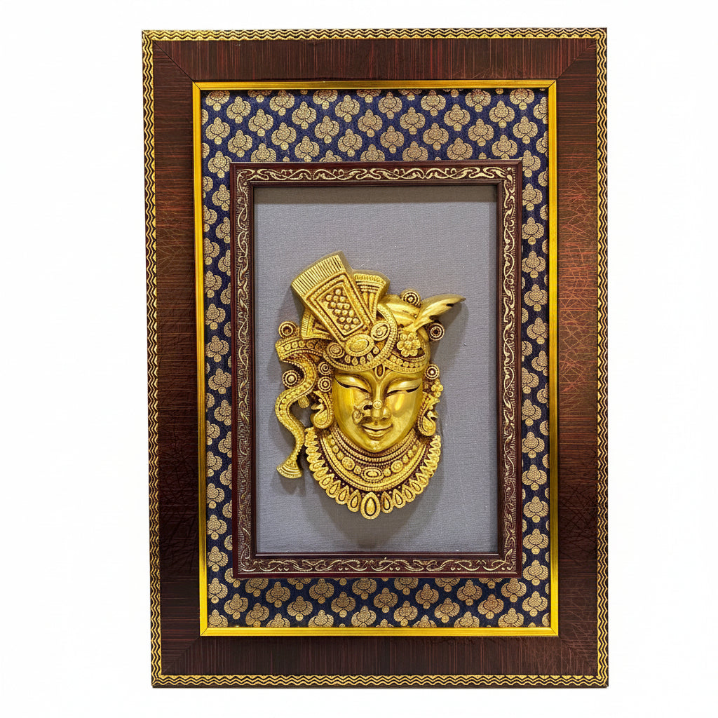 A framed decorative wall art piece featuring a gold-toned ornate mask or sculpture centered on a patterned navy and gold mat, set in a dark wood frame with gold trim.