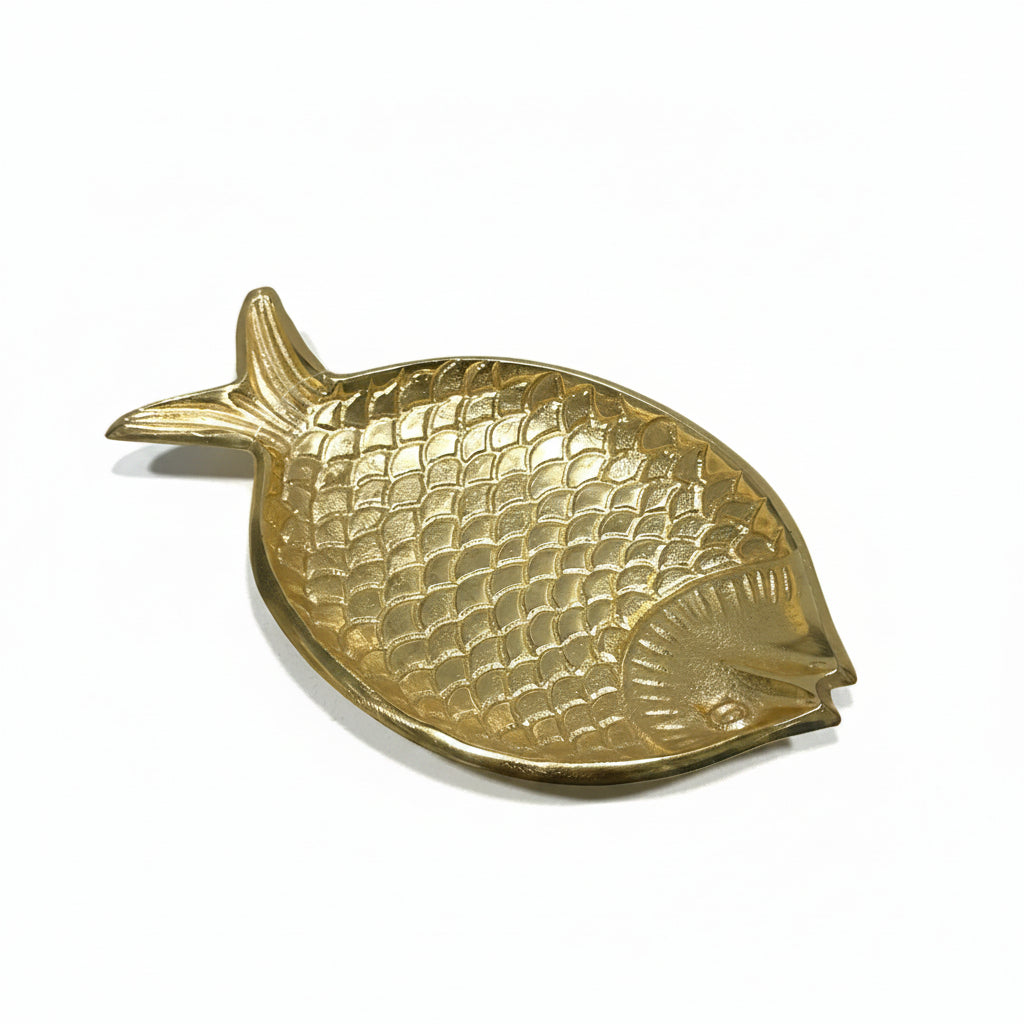 A gold-colored fish-shaped metal tray with a textured, scale-like pattern, photographed on a white surface.