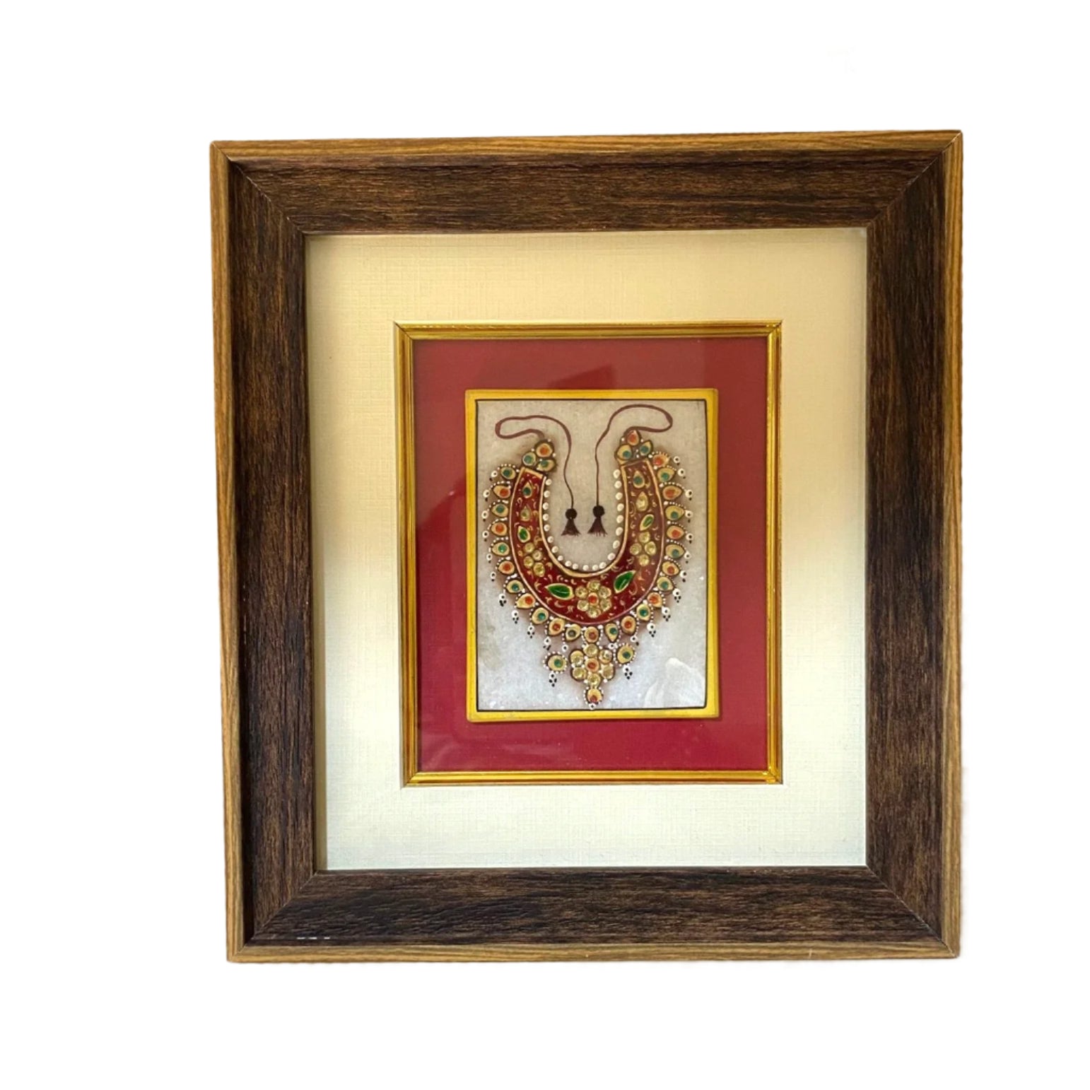Framed jewelry display with a decorative necklace on a textured wall.