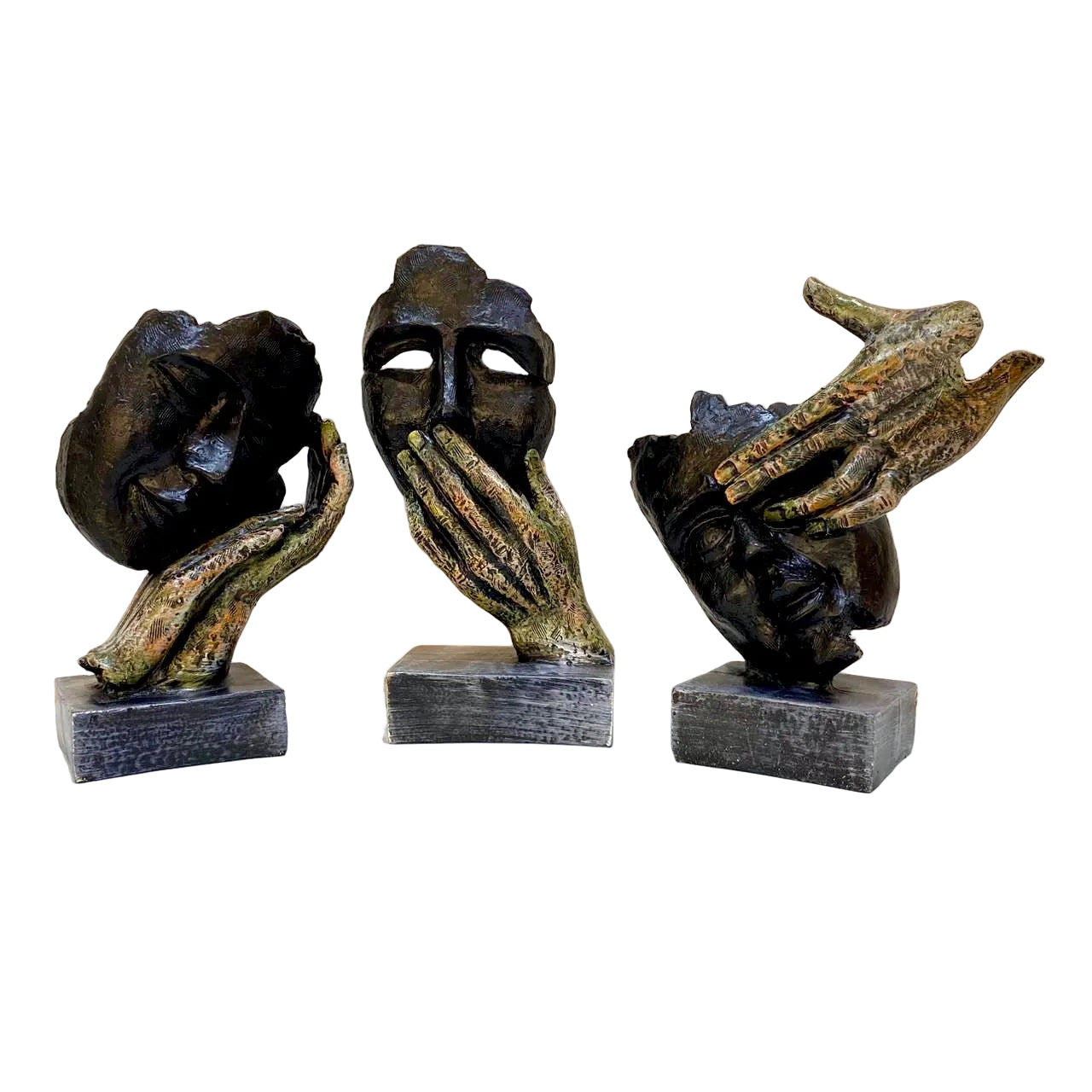 Three bronze sculptures of hands and masks on a white surface with a light-colored wall background.