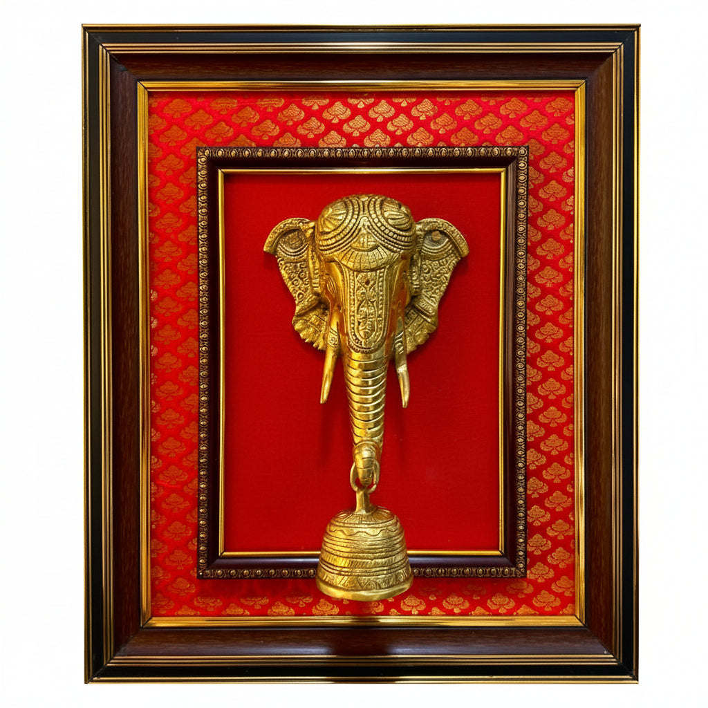 A framed decorative wall piece featuring a gold elephant head sculpture mounted on a red patterned background, enclosed in a dark wood and gold frame against a white textured wall.