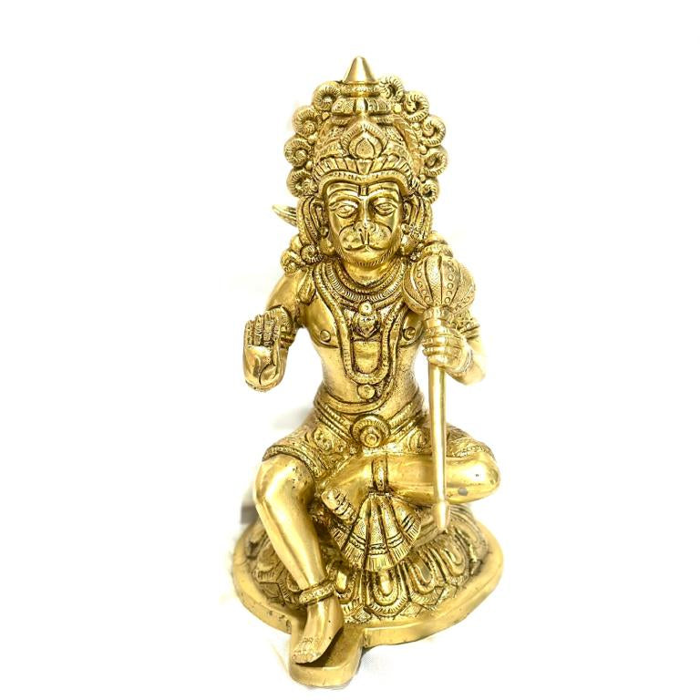 A gold-colored brass statue of Lord Hanuman, a Hindu deity, seated with a staff in his hand.