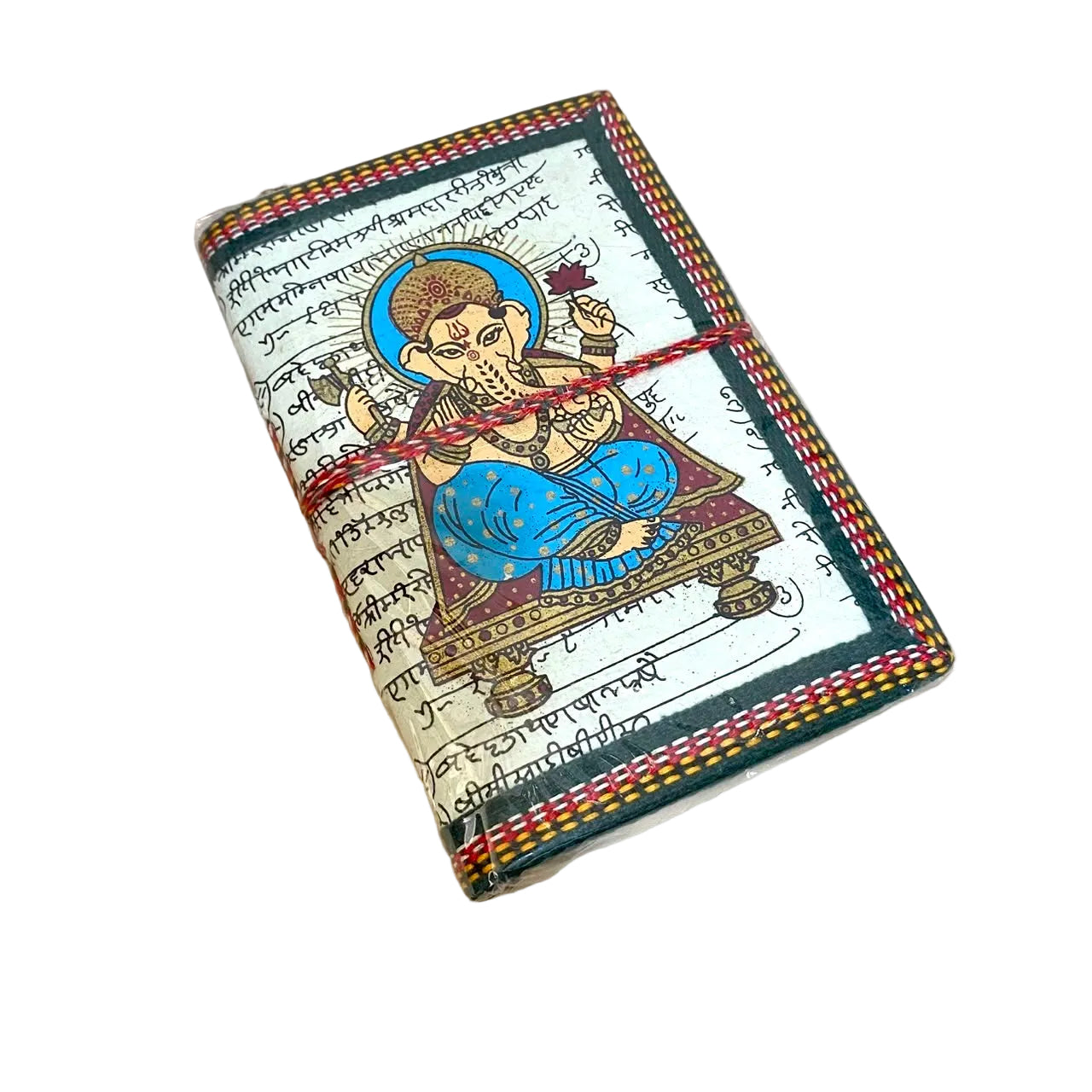 A small handmade notebook or journal with a colorful illustration of Lord Ganesha on the cover, wrapped with a red string closure, resting on a light wood surface.