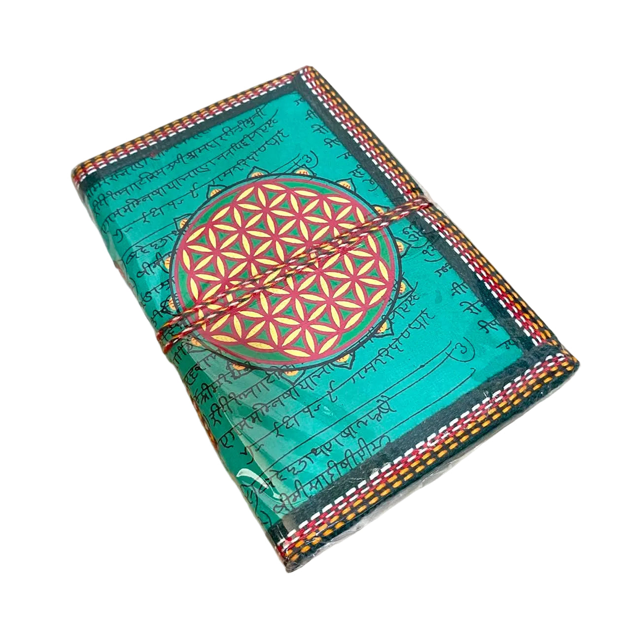 A handmade journal with a turquoise green cover featuring a large red and yellow geometric flower design in the center, surrounded by black script. The journal is wrapped with a brown cord and placed on a light wood surface.