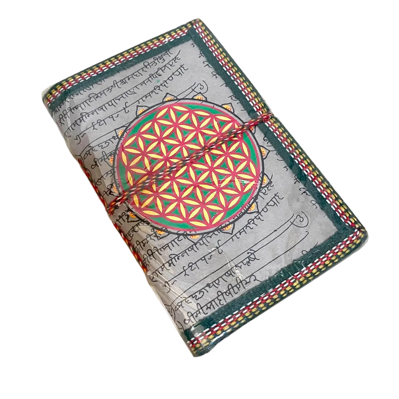 A handmade journal with a gray script cover, decorated with a colorful 'Flower of Life' motif and a red string tie, resting on a light wood surface.