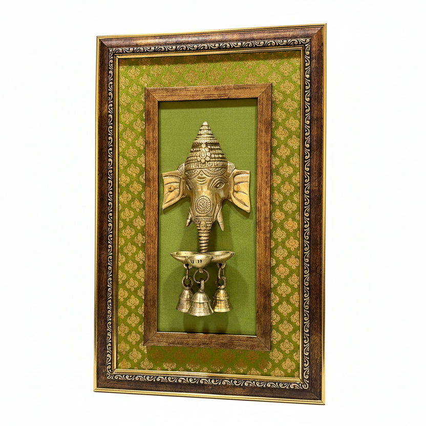 Decorative wall art with a gold Ganesh head and bells on a green background, framed in brown.