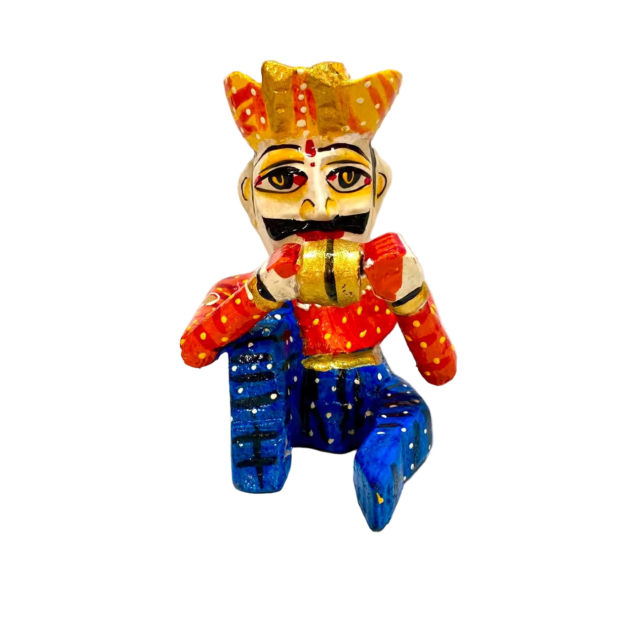 A hand-painted wooden folk art figurine of a seated figure with a gold crown, red and orange patterned top, and blue pants, set against a plain off-white background.