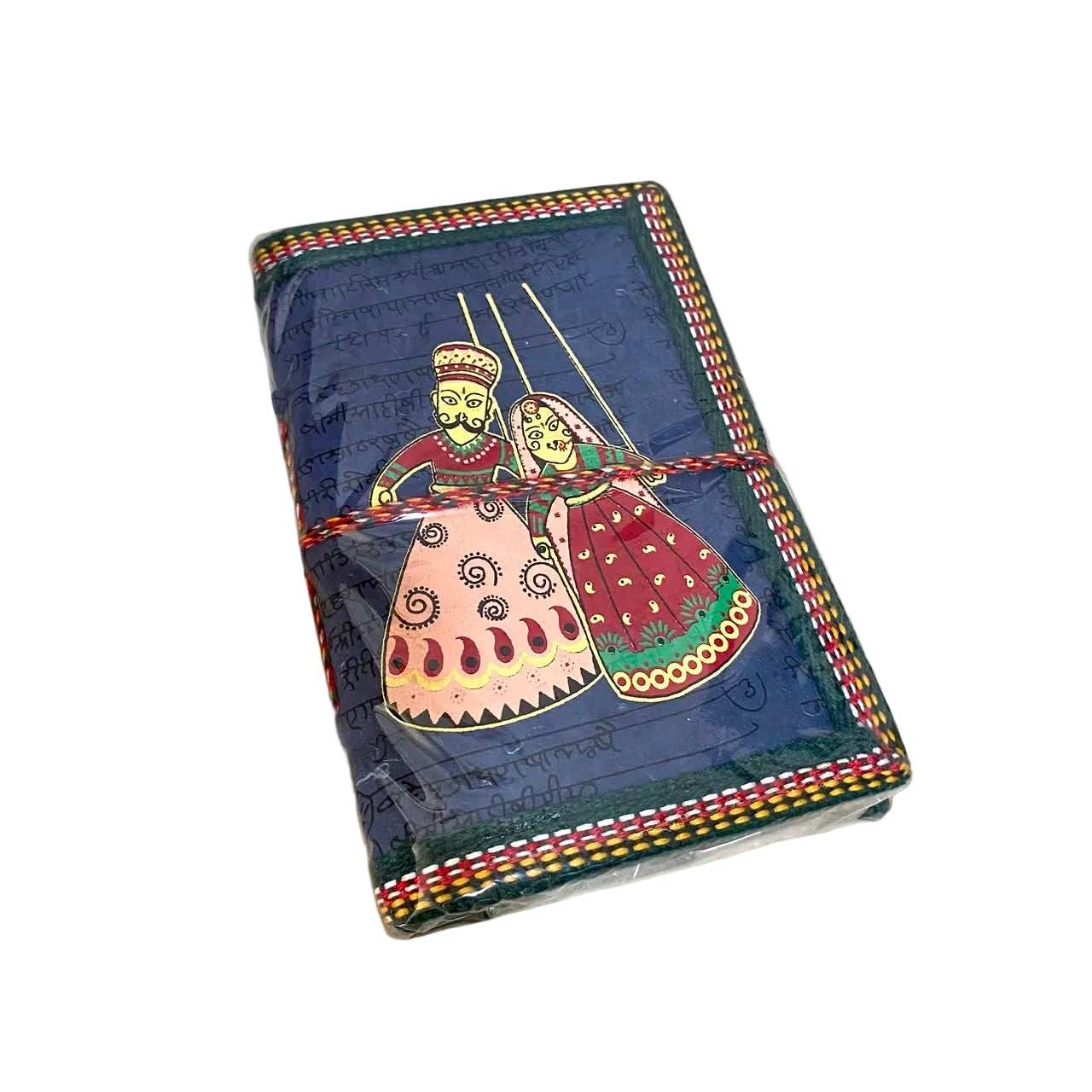 A handmade leather journal with a dark blue cover featuring traditional folk art illustrations of a couple, wrapped with a red and yellow patterned cord, resting on a light wood surface.