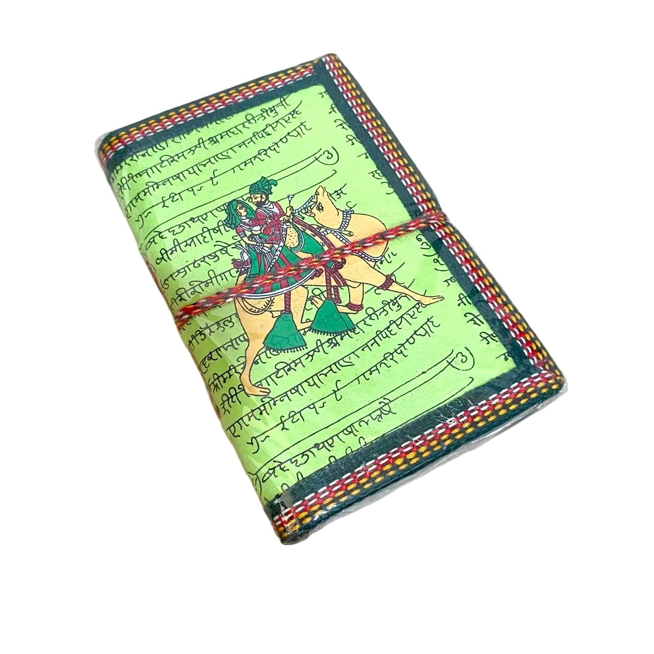 A handmade leather journal featuring a light green cover printed with black Devanagari script and an illustration of a horse rider on a yellow horse. The journal is wrapped with red and yellow string and has a decorative braided border, resting on a light wood surface.