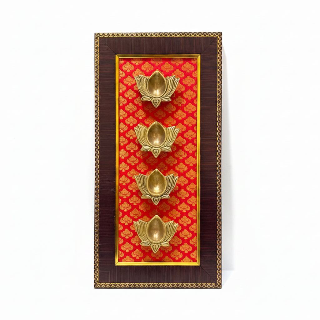 A decorative wall-mounted brass oil lamp holder featuring four gold-toned lotus-shaped brass lamps set against a red patterned background, enclosed in a dark brown wood frame with gold trim.