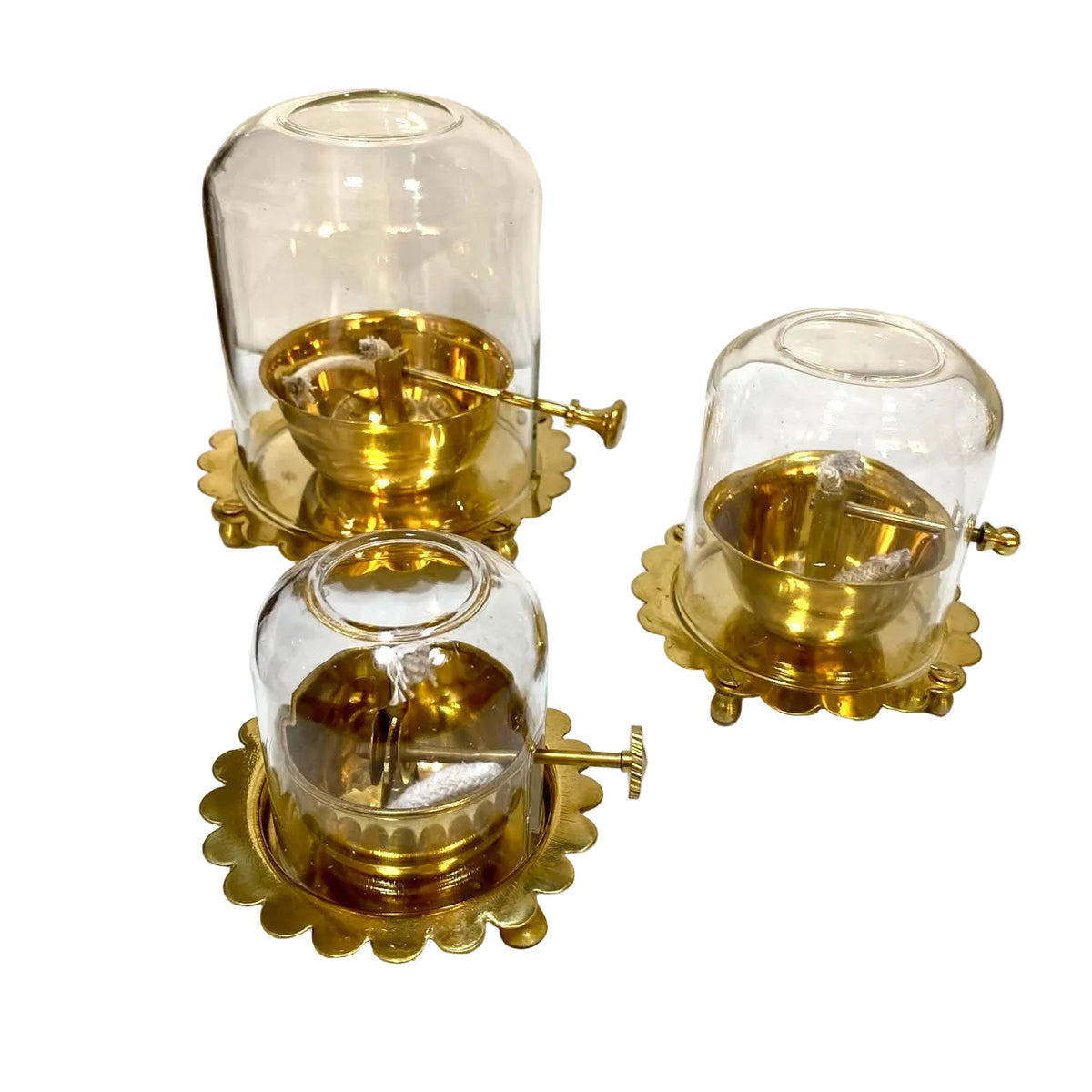 Three vintage brass and glass wind-up clock ornaments displayed on a white surface against a plain wall.
