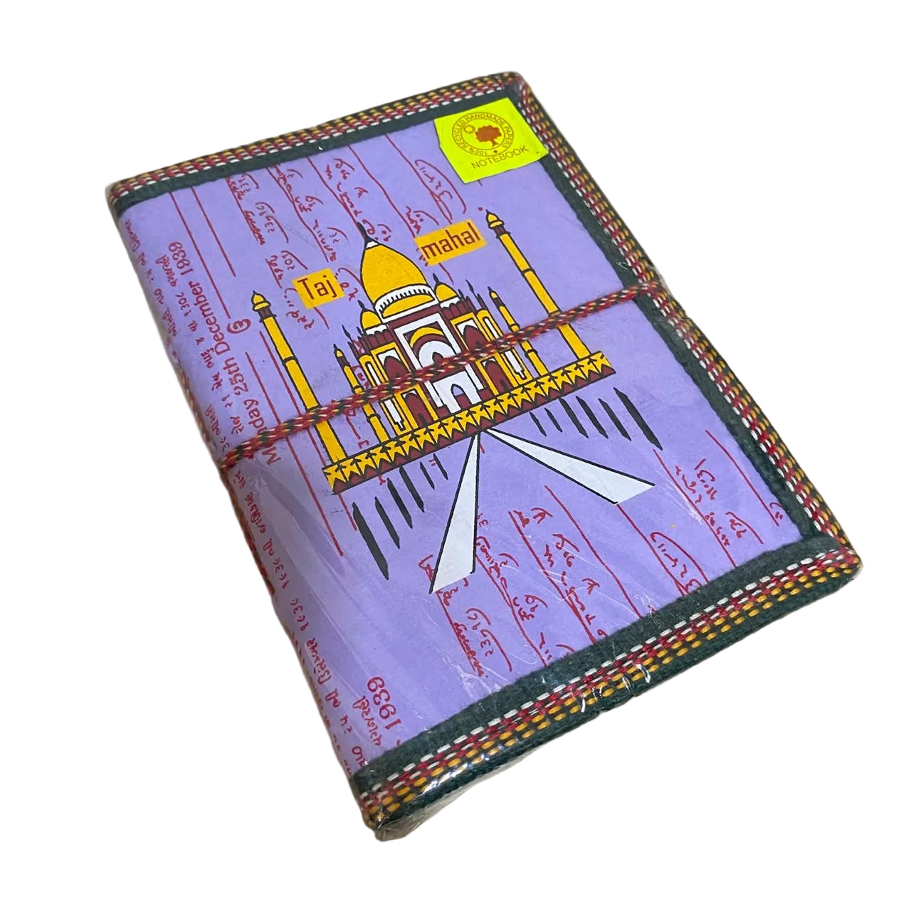 A handmade paper notebook featuring a purple cover printed with the Taj Mahal, Hindi calligraphy, and a red string wrapped around it, resting on a light wood surface.