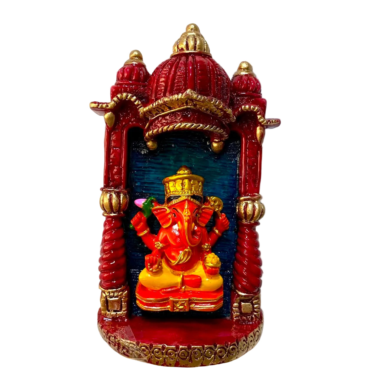 A small decorative wall-mounted idol of Lord Ganesha seated inside a red and gold miniature temple niche, photographed against a white textured wall.