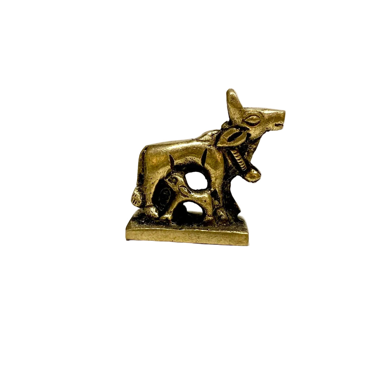 A small brass figurine of a cow and calf standing on a rectangular base, photographed on a white tabletop with a blurred indoor background.