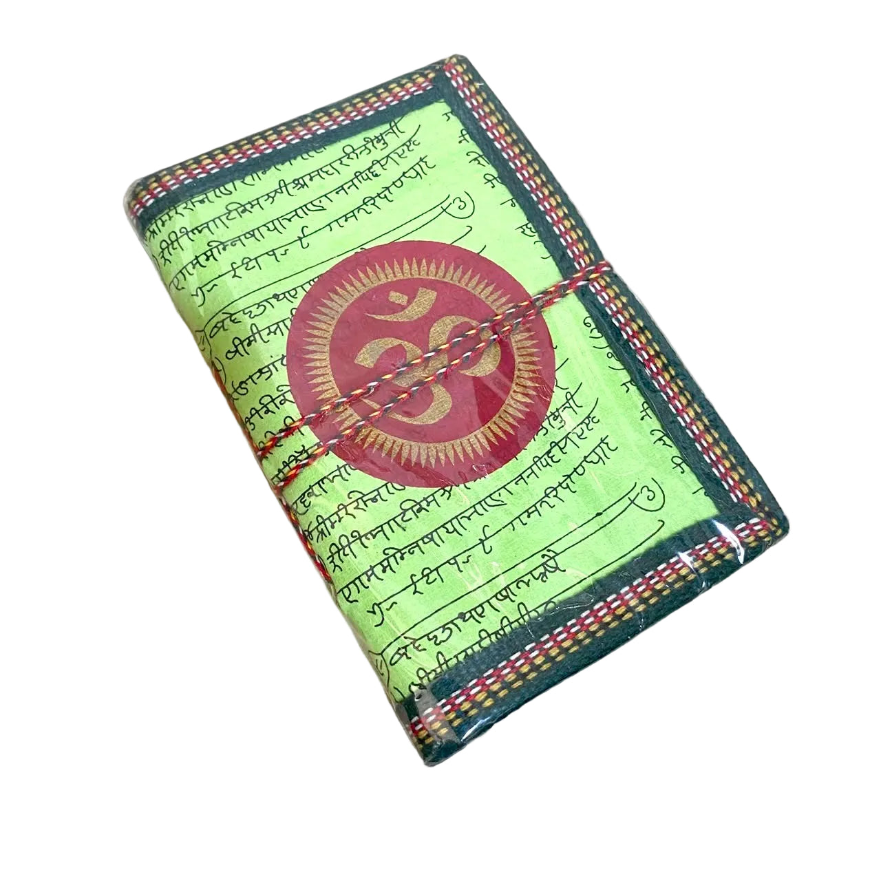 A small fabric-covered notebook or journal with a green cover, printed script, red stitched borders, and a large red circular Om symbol on the front, photographed on a light wood tabletop.