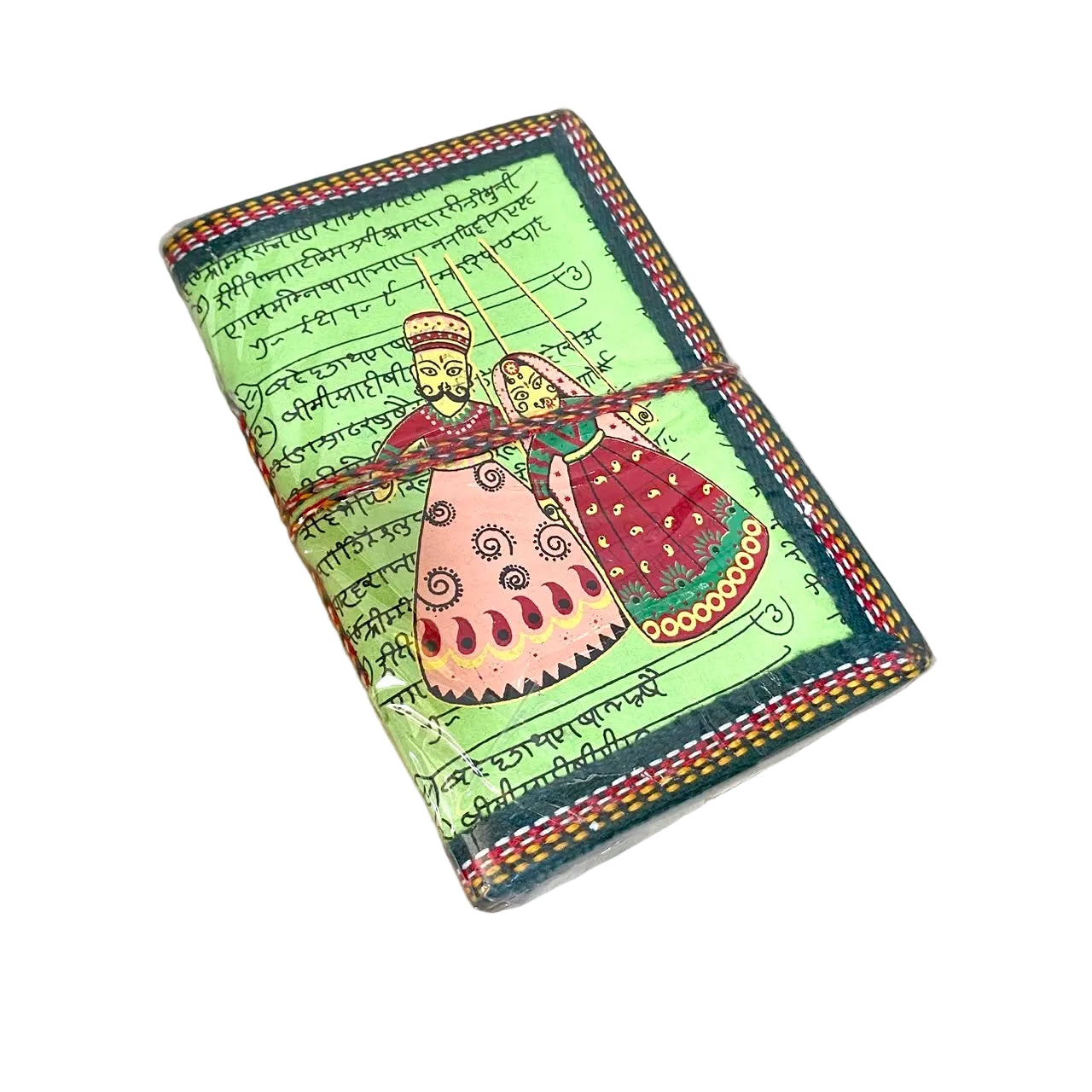 A small handmade notebook or journal with a light green cover, decorated with traditional folk art of a couple in colorful clothing, surrounded by script and a patterned border. The notebook is tied with a red string and rests on a light wood surface.