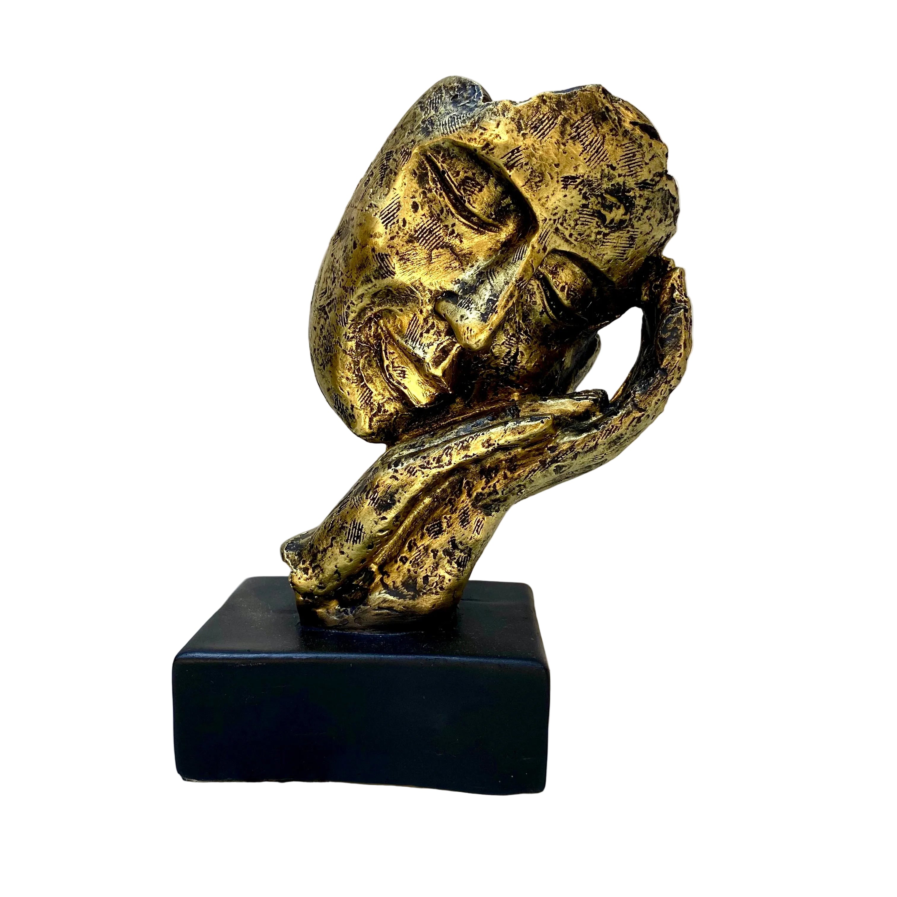 Gold sculpture of a face on a black base against a white wall