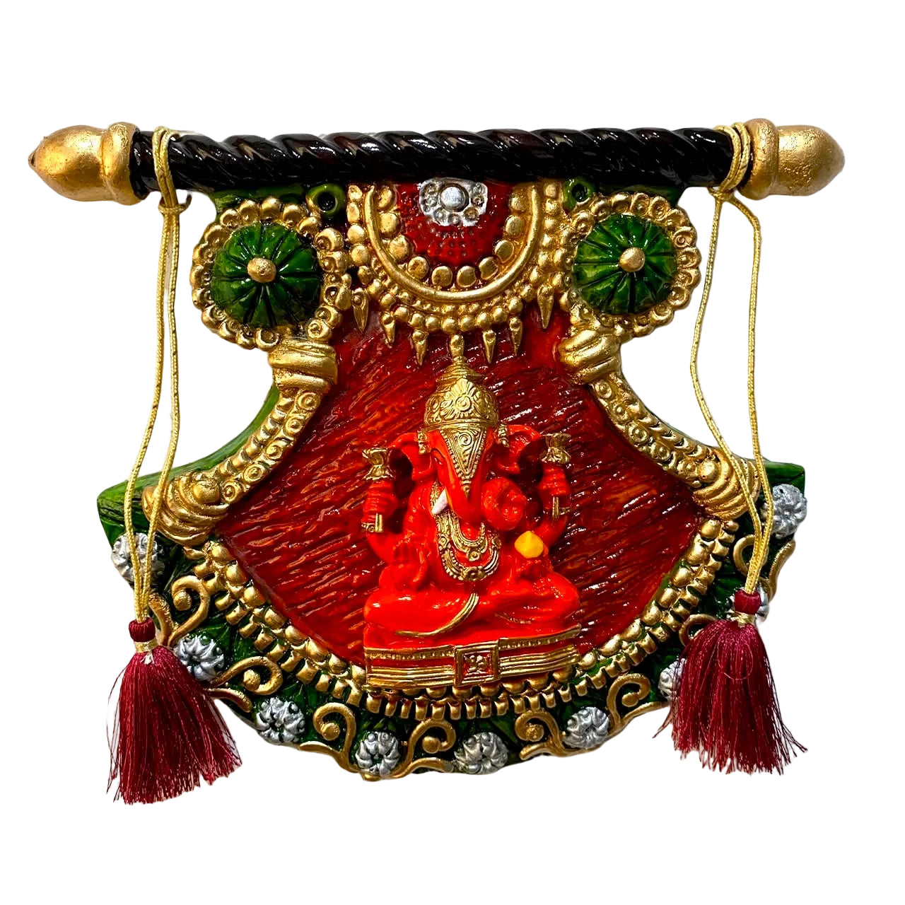 A decorative hanging wall plaque featuring a red Lord Ganesha figure, ornate gold detailing, green accents, and tassels, mounted on a textured white wall.