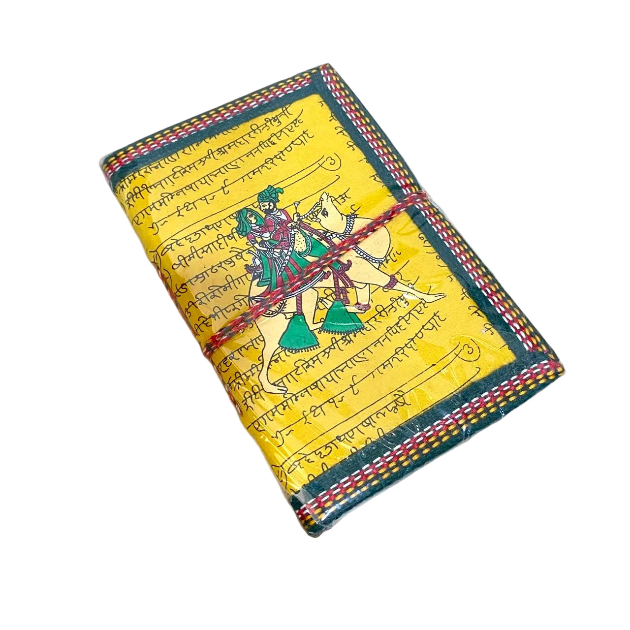 A handmade yellow notebook or journal with Devanagari script and a colorful illustration of Lord Krishna and Arjuna on horseback, wrapped with a red string closure, resting on a light wood desk.