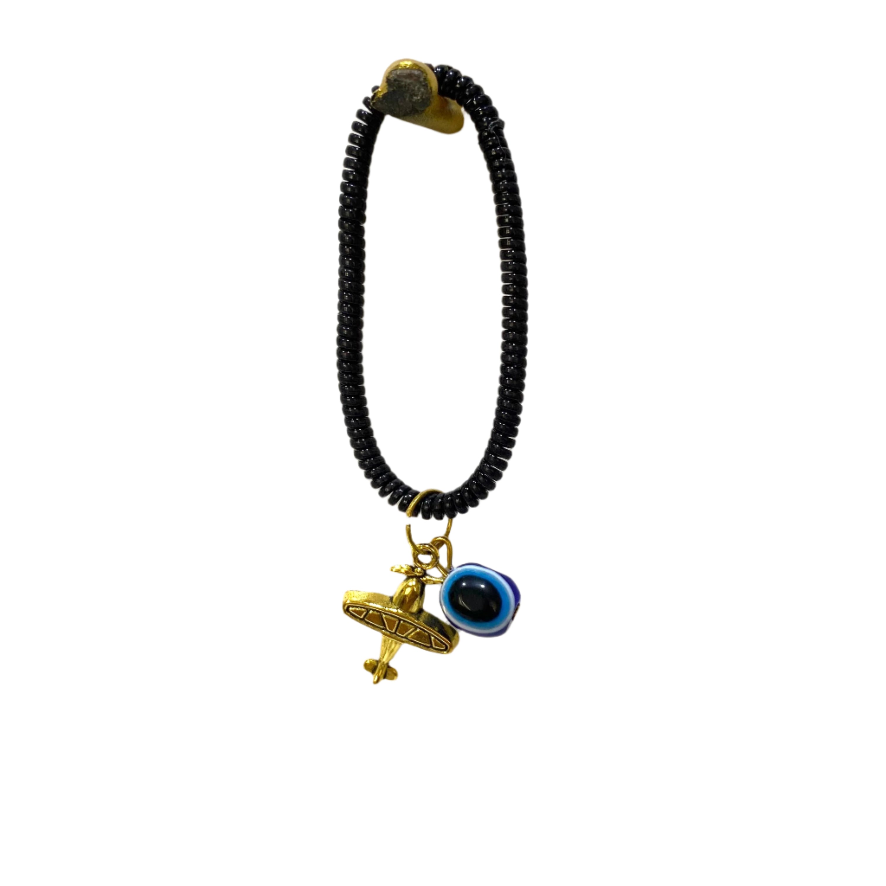 Black beaded bracelet with gold airplane charm and blue evil eye charm on a textured white background