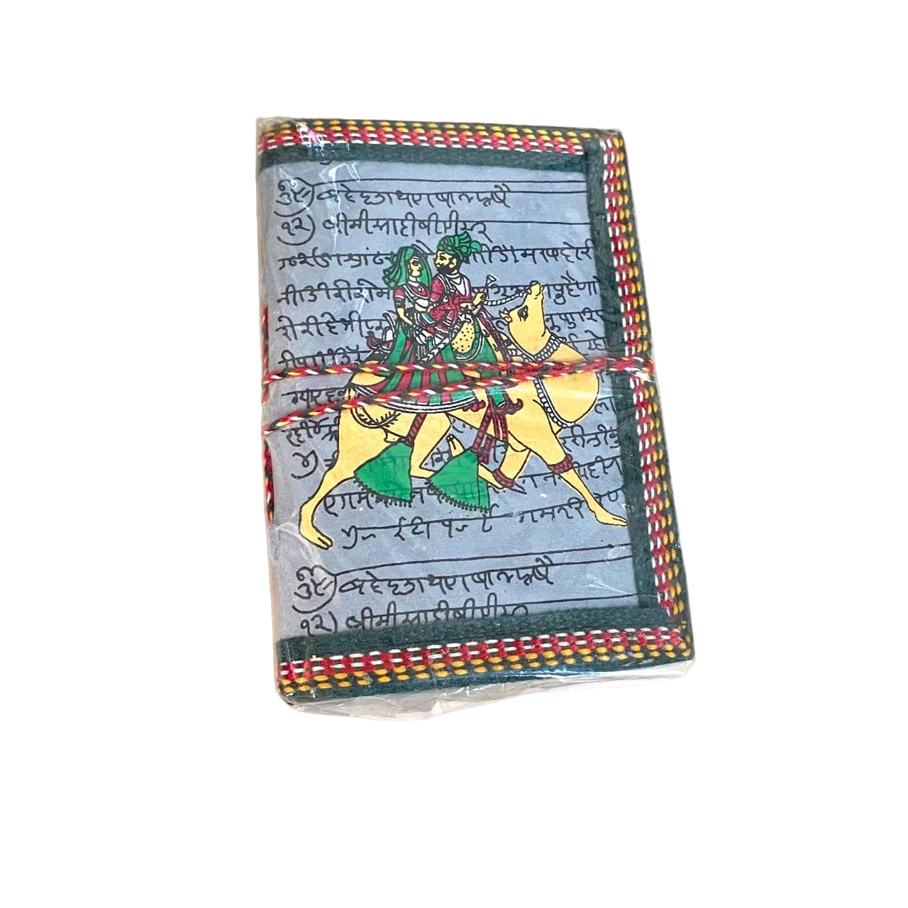 A small rectangular notebook or journal with a gray cover printed in Devanagari script, decorated with a colorful illustration of a figure on a yellow camel and wrapped with a red-and-yellow striped cord, placed on a light wood surface.