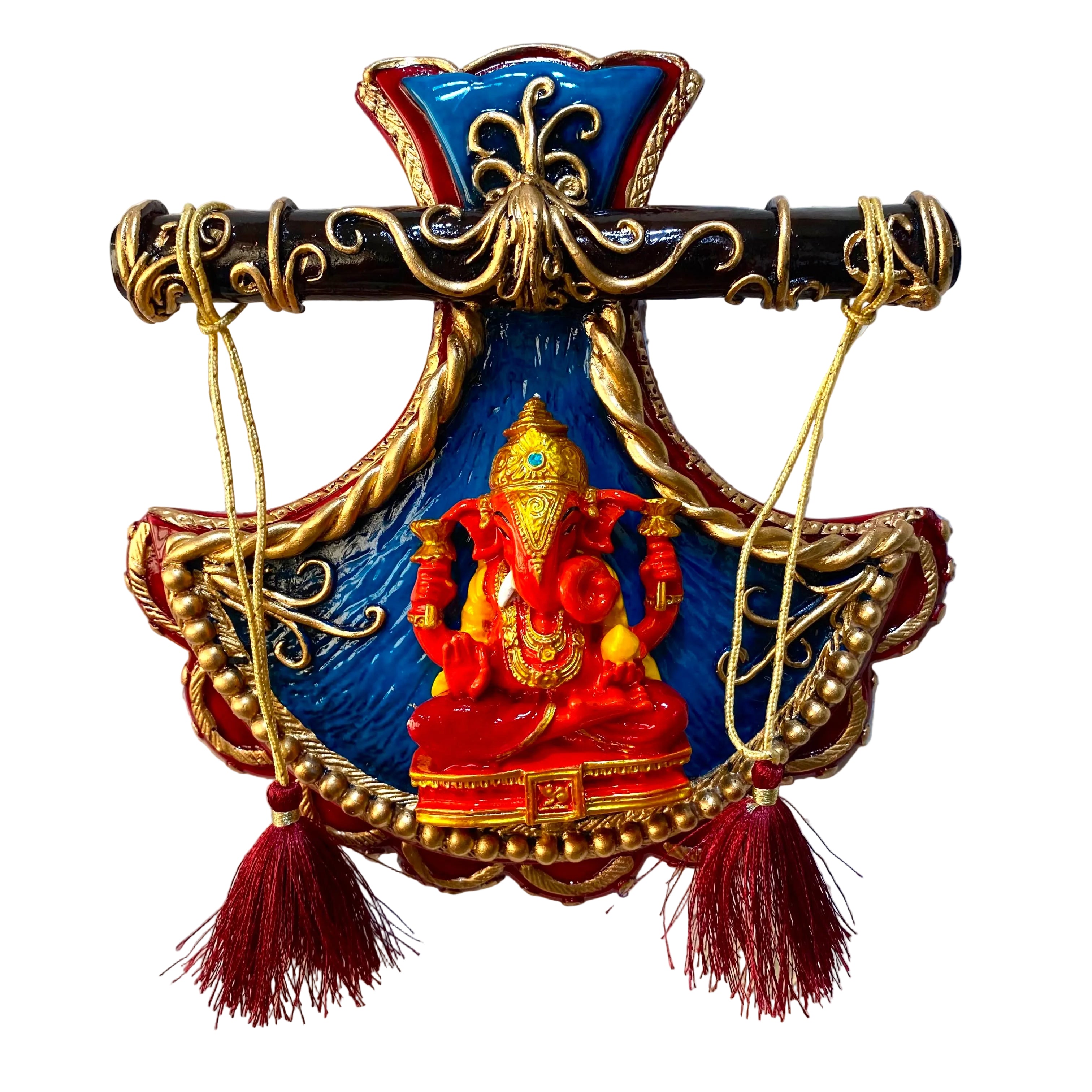 A decorative wall hanging featuring a red and gold Ganesha statue on a blue and red shield-like base, with a black and gold horizontal bar across the top and two red tassels hanging from gold cords, shown against a white textured wall.