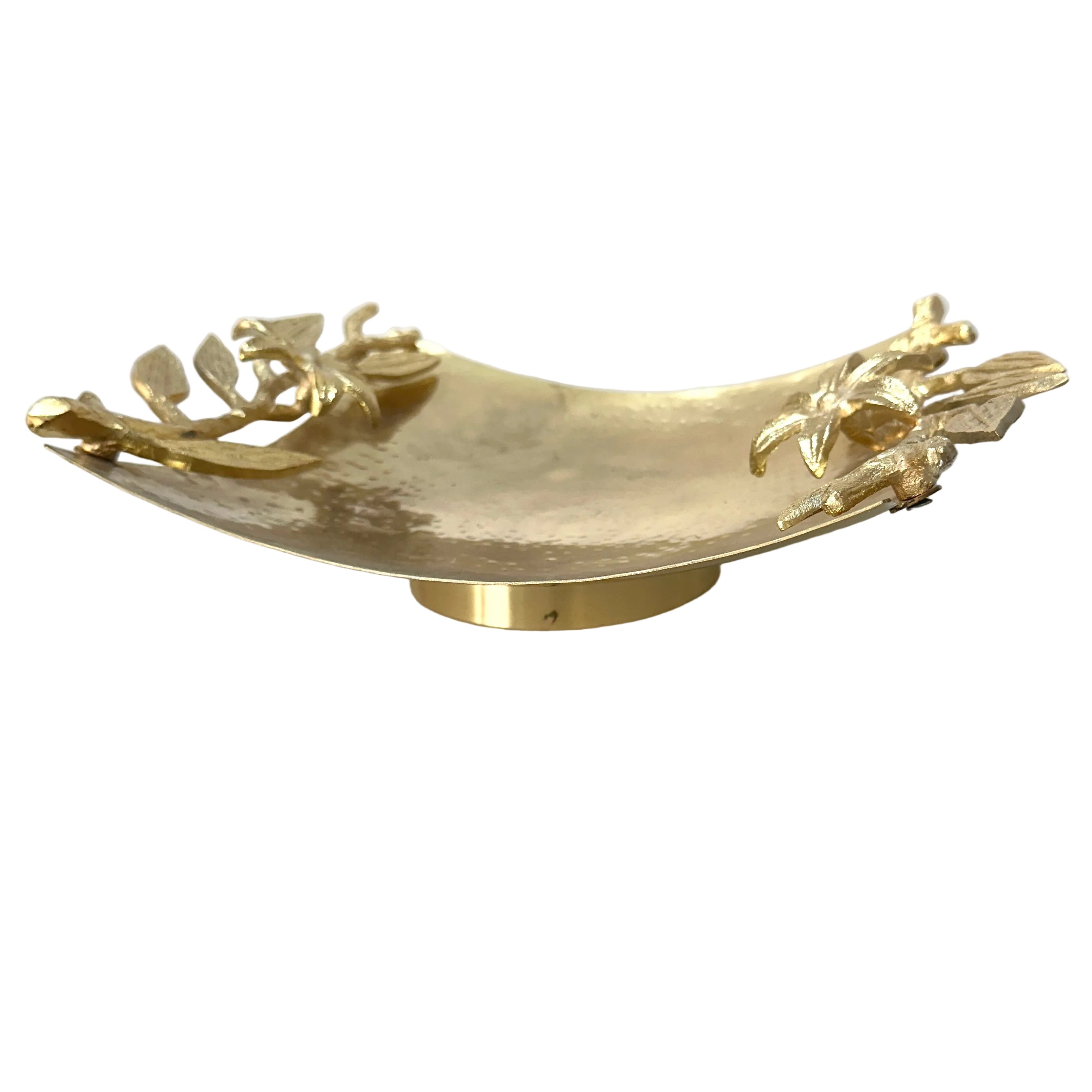 A gold-toned metal decorative bowl with sculpted cherub figures on the raised edges, shown on a white tabletop against a light wall.