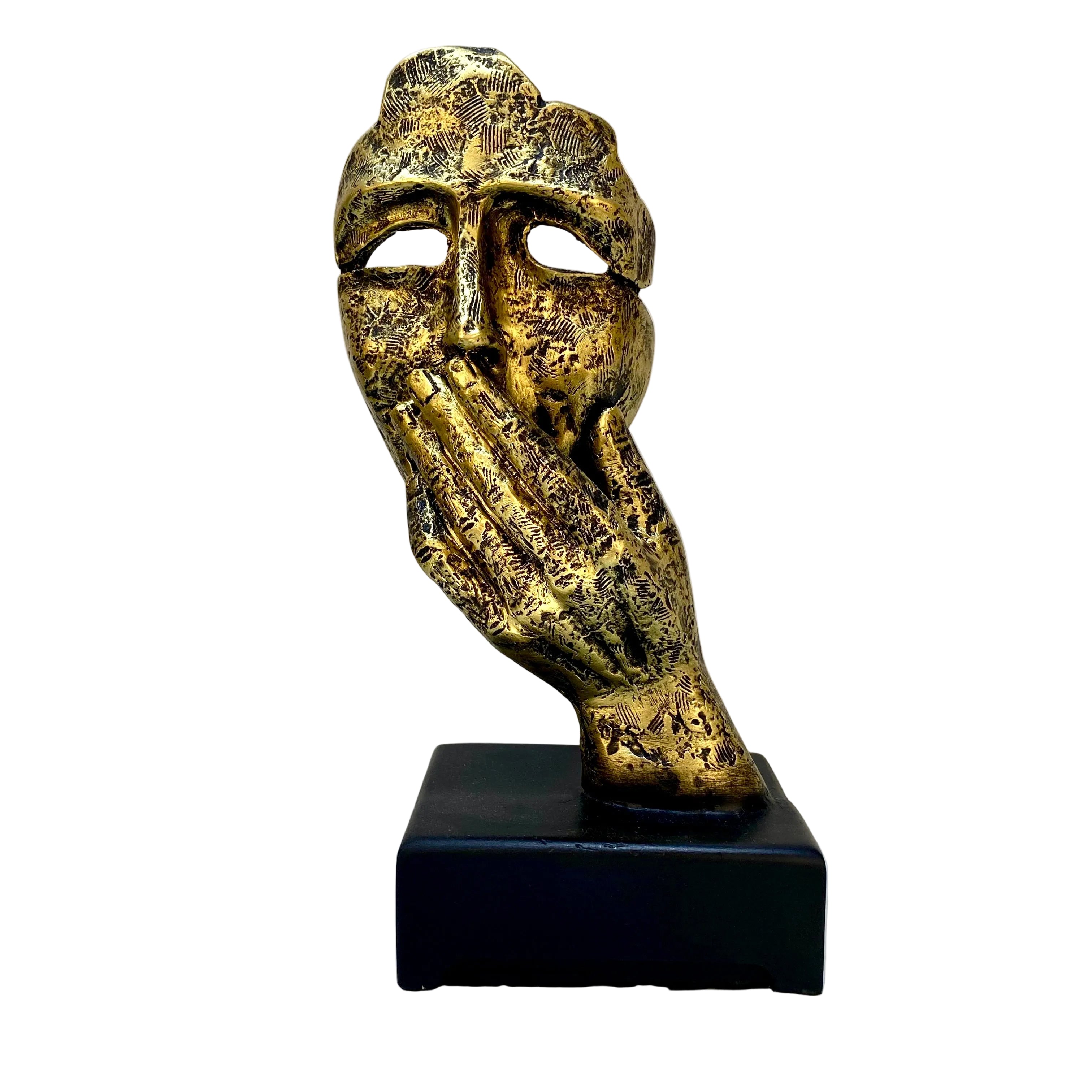 Decorative mask sculpture on a black base against a white wall with visible wear.