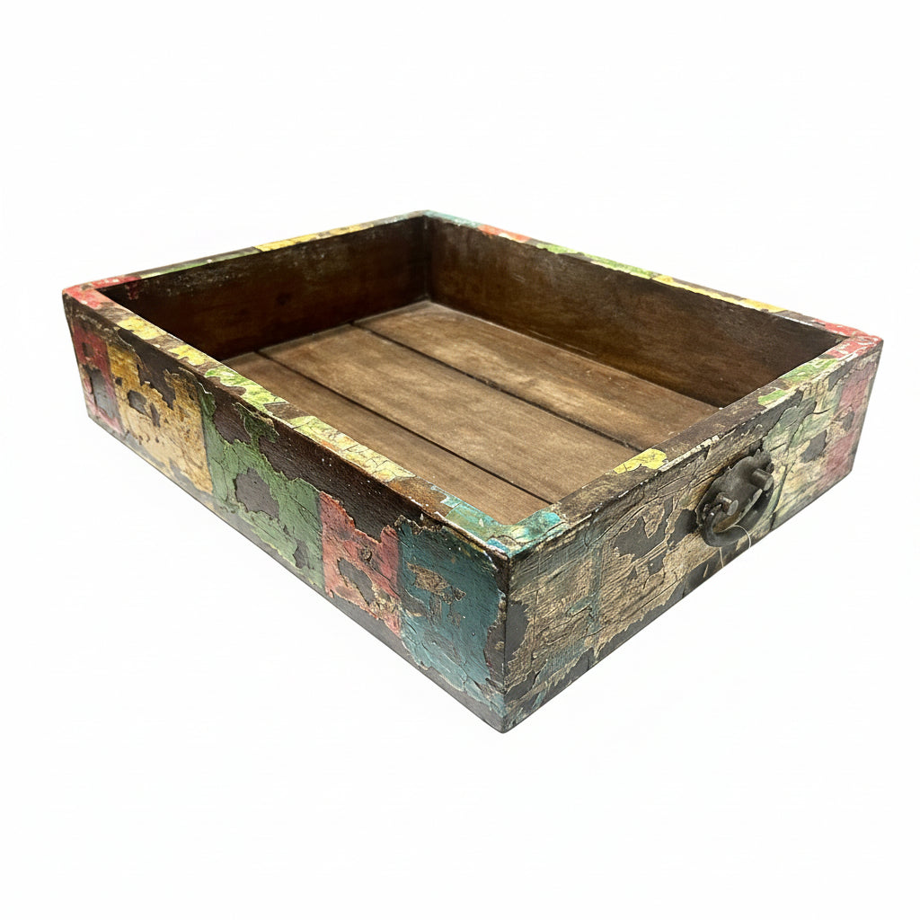 A rustic rectangular wooden box with a distressed multicolor paint finish and a dark metal handle, sitting on a white table in a workshop setting.