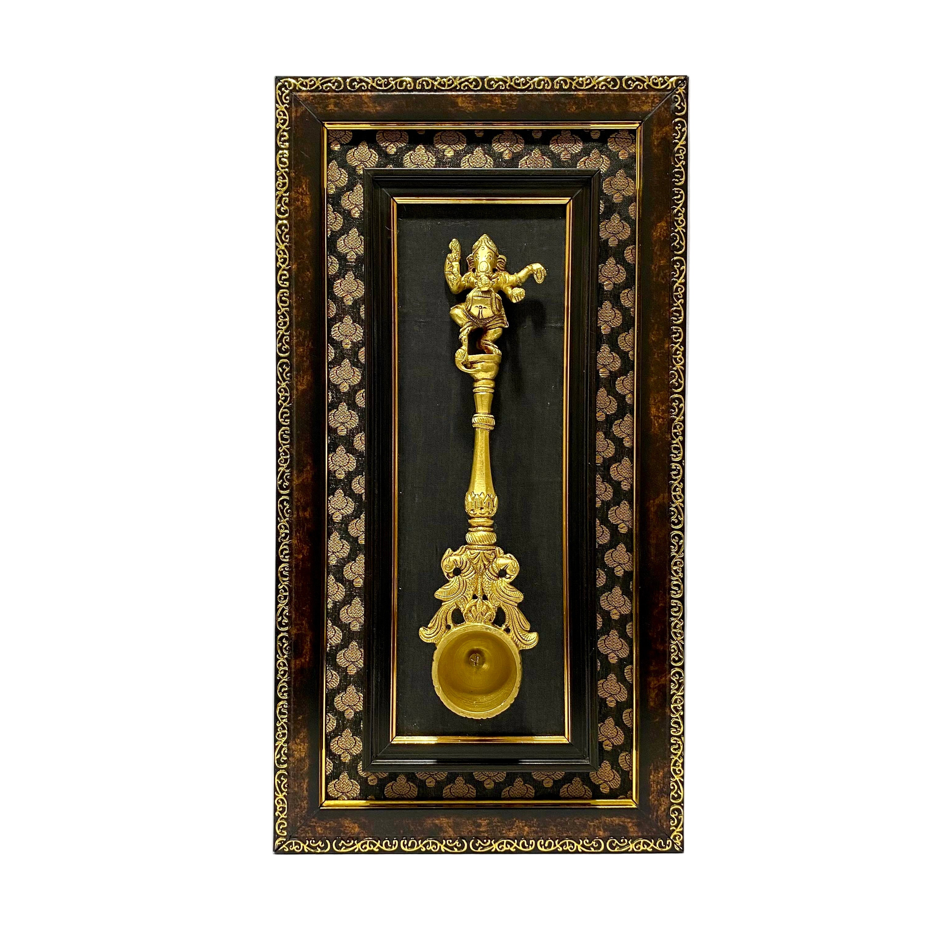 Decorative wall art with a gold figurine and bell in an ornate black frame.