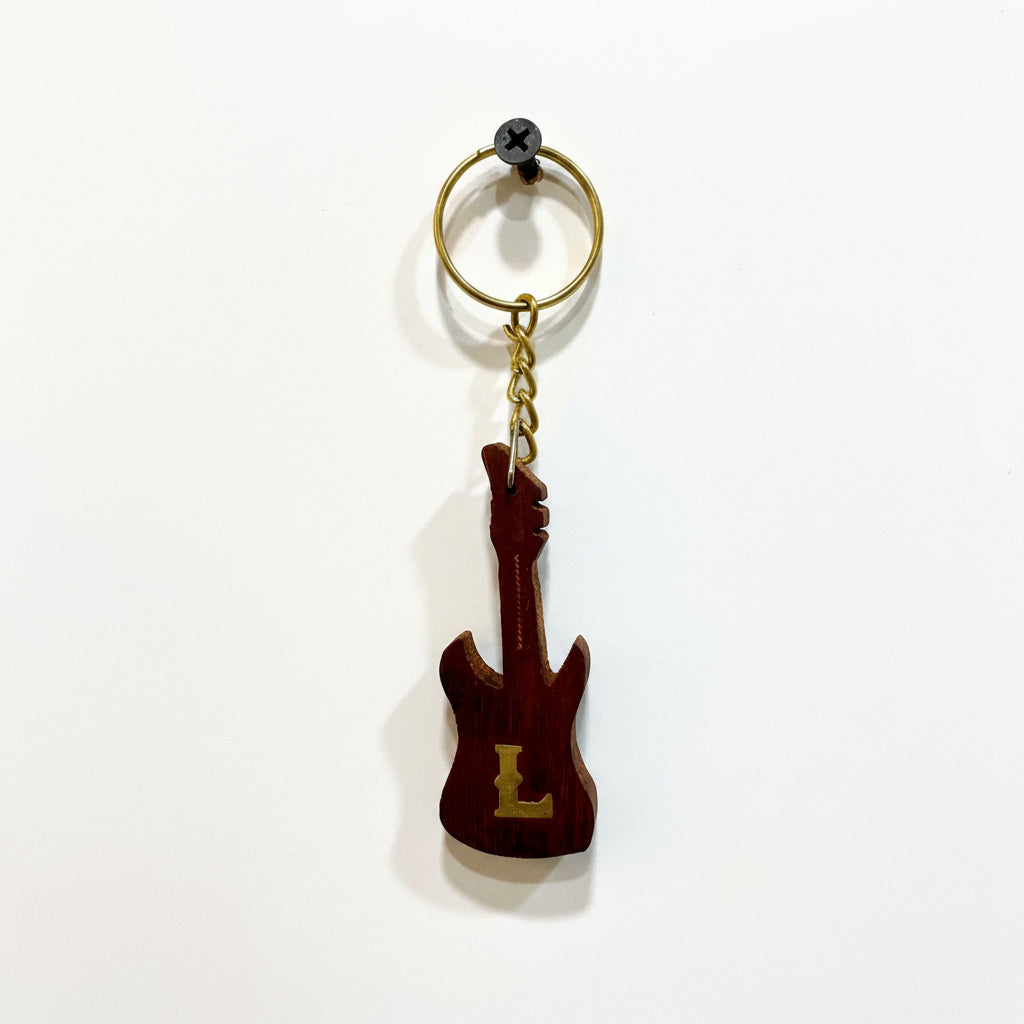 Guitar-shaped keychain with a letter 'L' on a textured white background