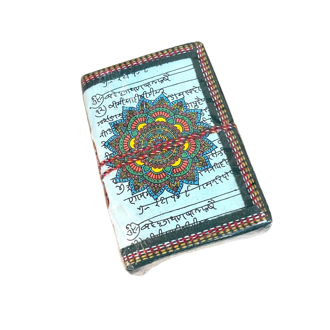 A small notebook or journal with a white cover, black script, and a colorful mandala design in the center, wrapped with a red and multicolor string, resting on a light wooden table.
