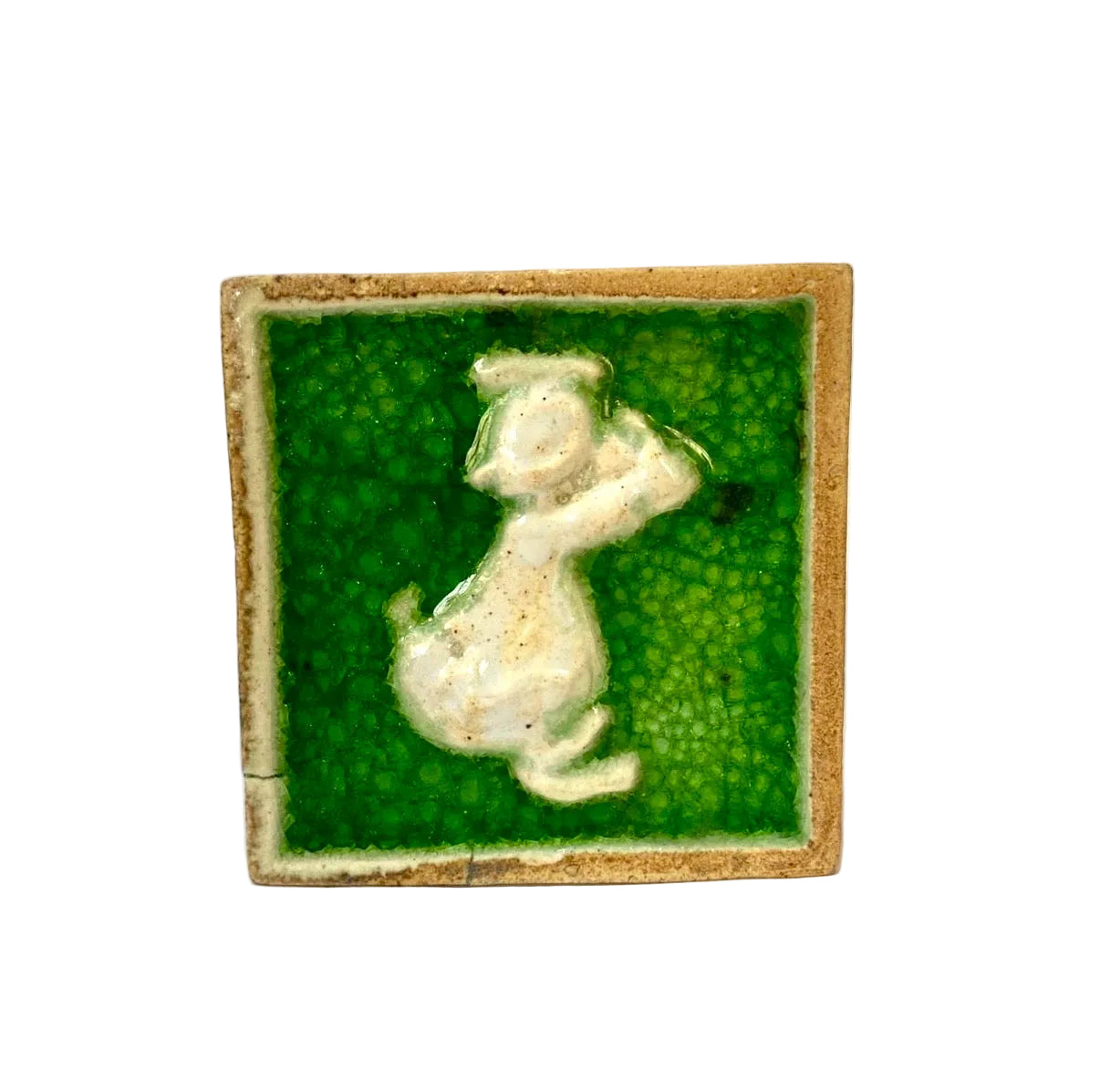 Small ceramic tile with a green background and white figure on a white surface