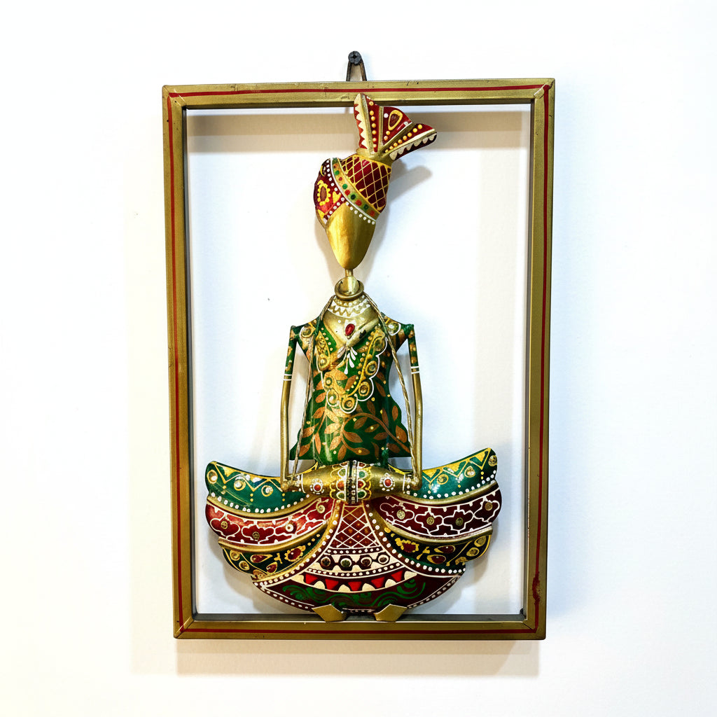 Decorative wall art with a gold and green figure in a frame on a textured white wall.