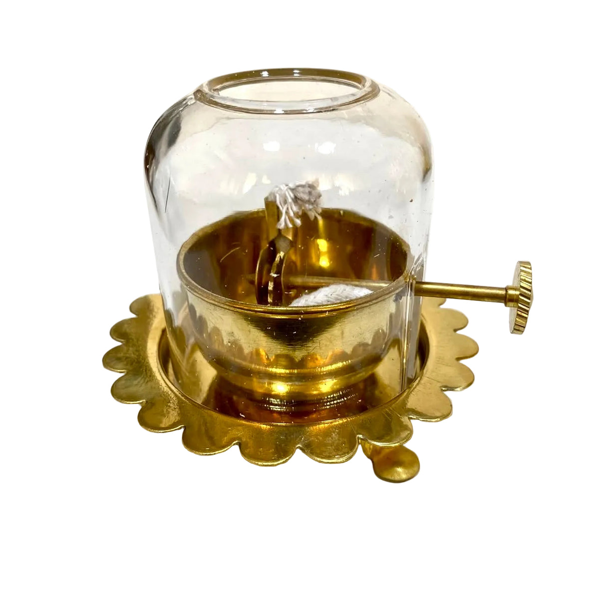A vintage brass and glass oil lamp with a scalloped brass base and a side adjustment knob, photographed on a white tabletop.