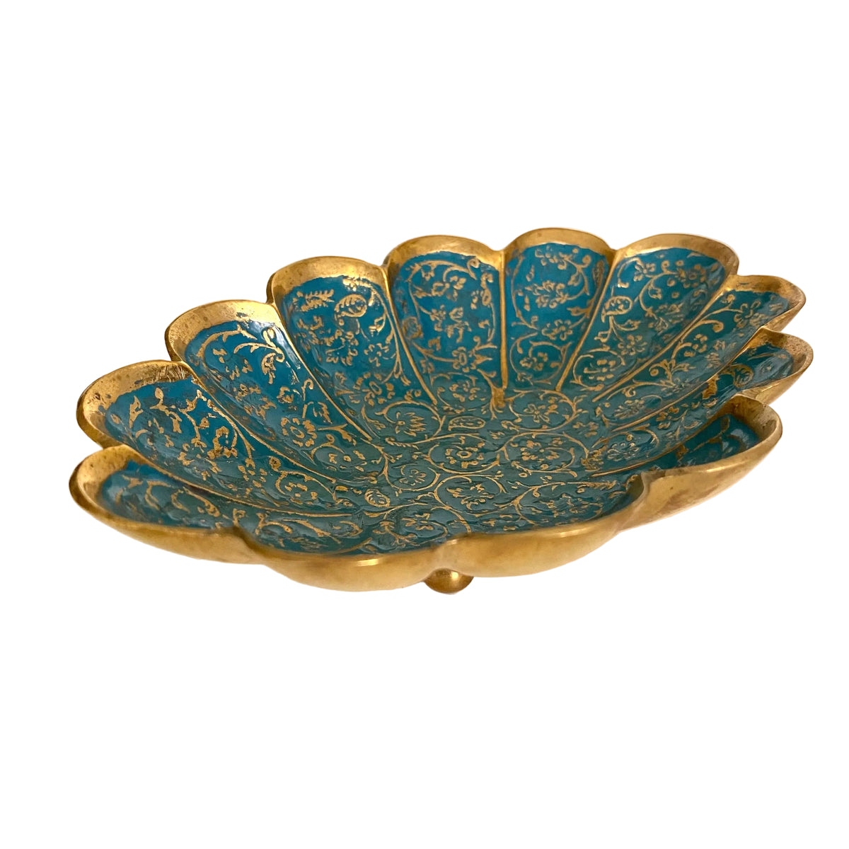A scalloped gold-toned metal dish with turquoise blue enamel panels and intricate gold floral patterns, resting on a light-colored tabletop.