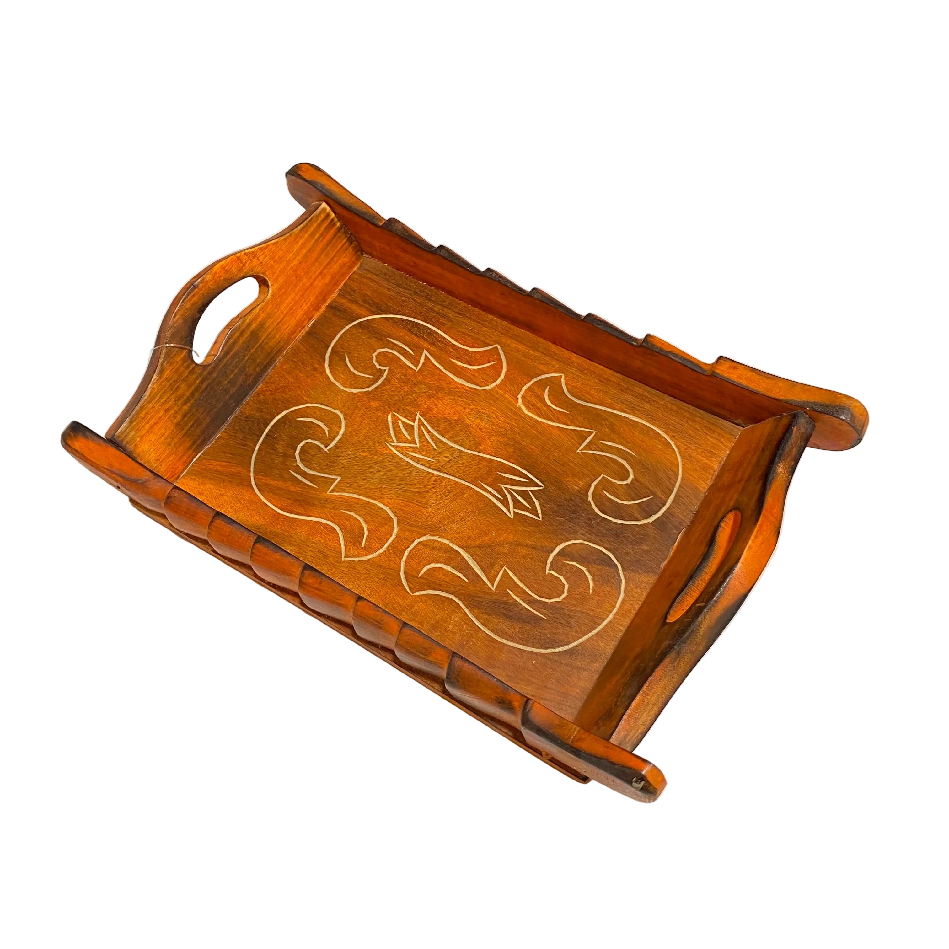 A rectangular wooden serving tray with integrated handles and carved scrollwork designs on the top, resting on a white table.