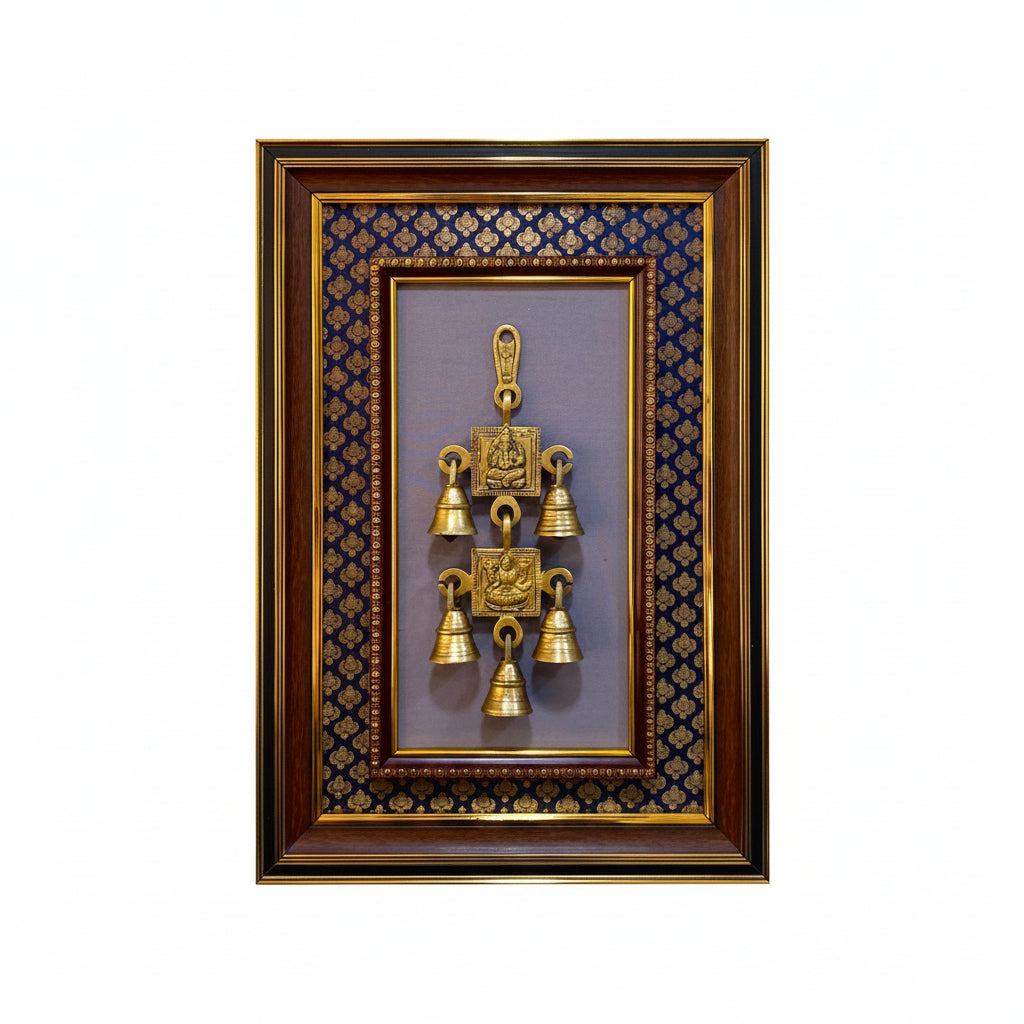 A framed decorative wall hanging featuring a central brass bell ornament with carved details, set against a purple background with a blue and gold patterned inner border, all enclosed in a dark wood frame with gold trim, mounted on a textured off-white wall.