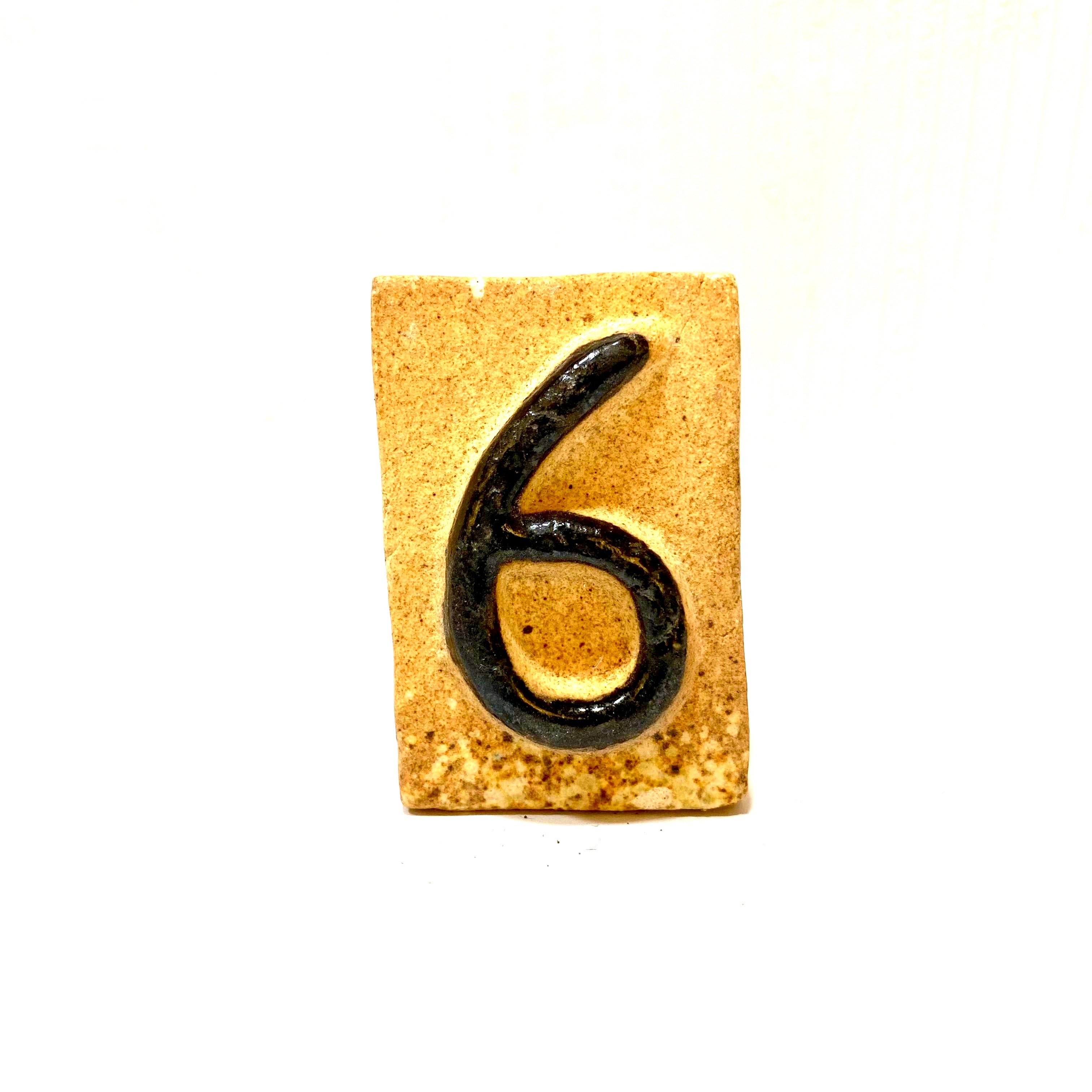 Number 6 embossed on a textured beige surface with a white background