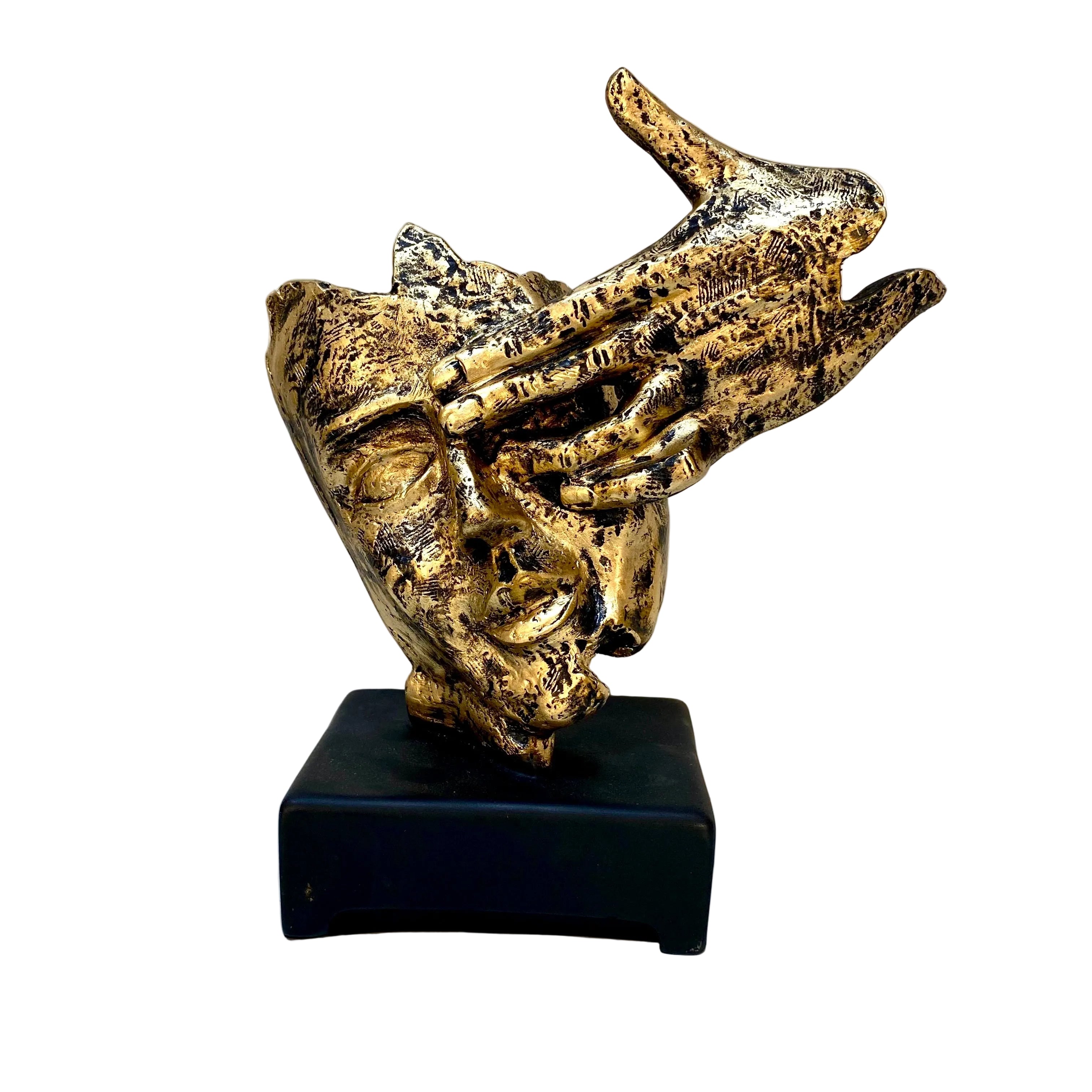 Gold-colored sculpture of a face with outstretched hands on a black base against a white background.
