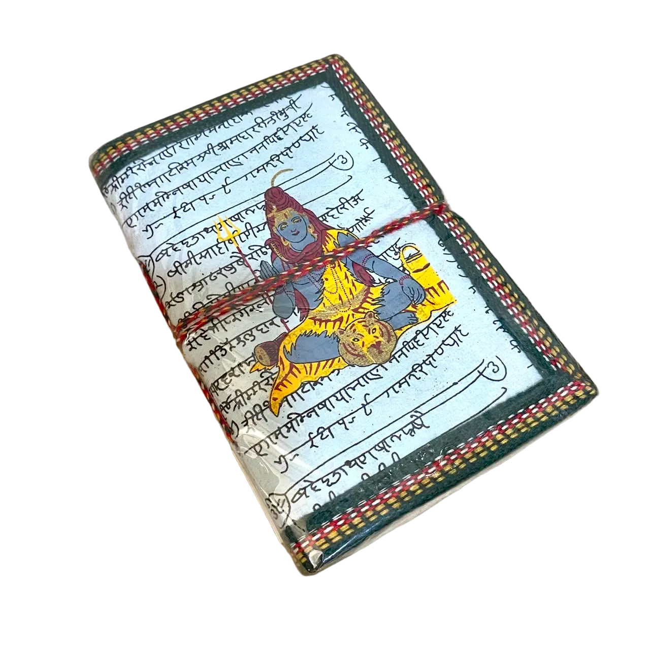 A small rectangular notebook or journal lying on a light wood surface. The cover has a cream background with black script, a colorful illustration of a seated figure in yellow and blue, and a dark green border with red and yellow striped accents.