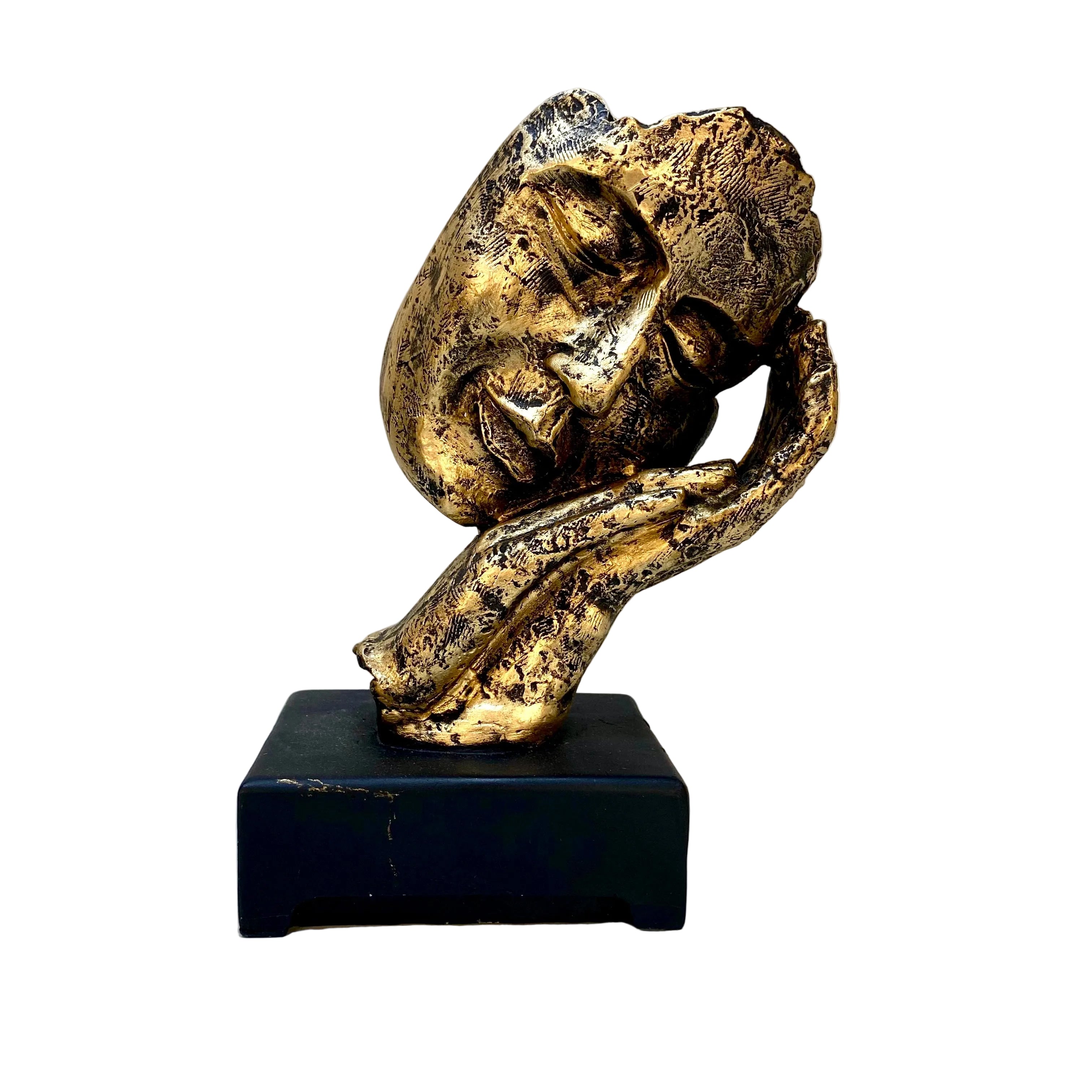 Gold sculpture on a black base against a white wall with visible wear.