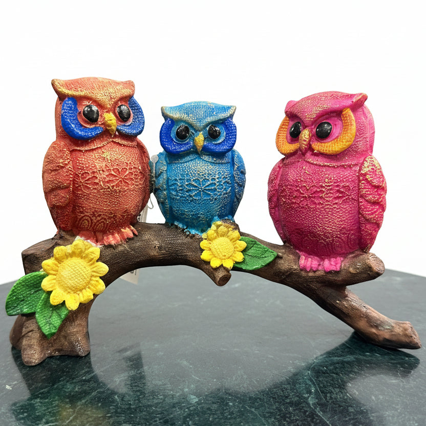 Three colorful owl figurines on a branch with flowers in a store setting