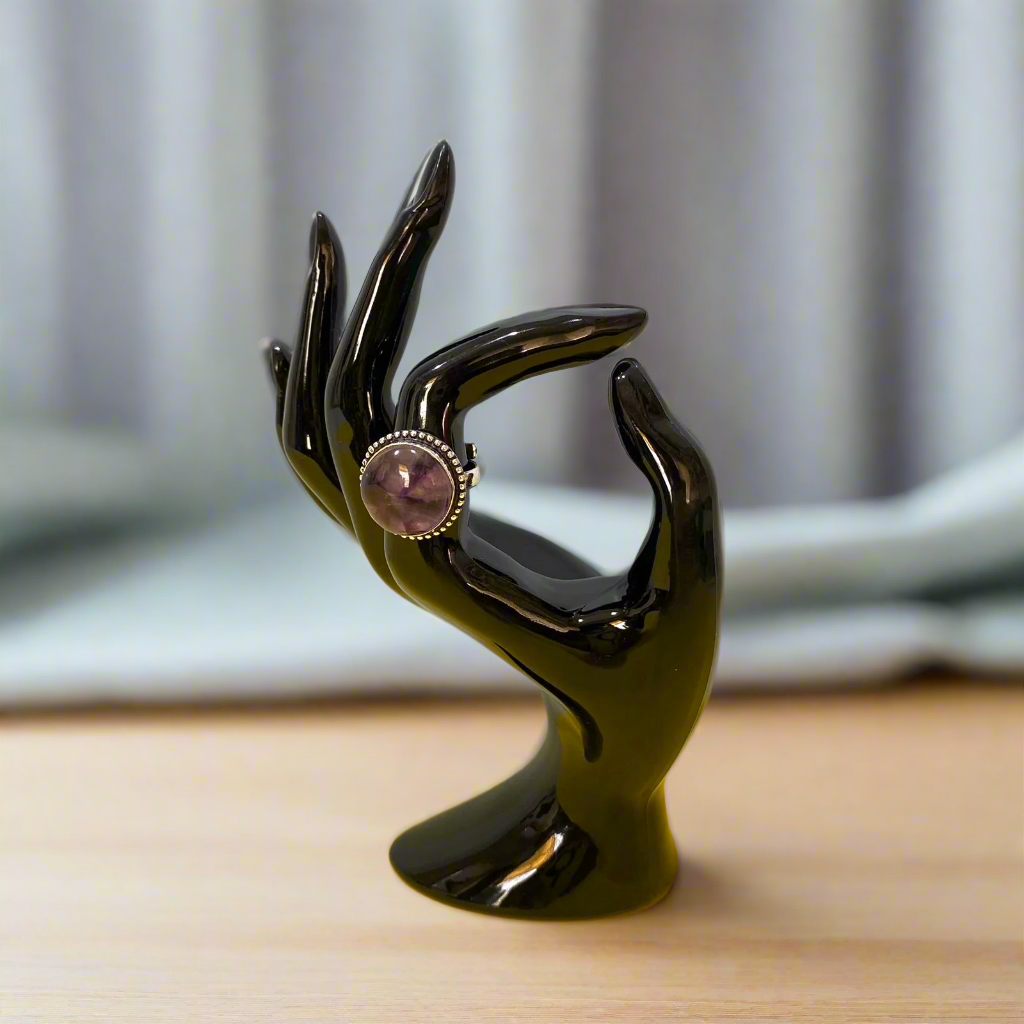 Black hand-shaped jewelry stand with a pink gemstone on a yellow surface