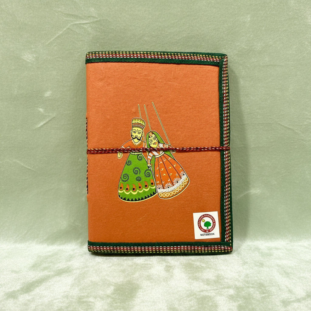 An orange handmade leather journal with a hand-painted folk art illustration of a couple in traditional clothing, bound with a red-and-white cord and finished with green and red patterned trim.