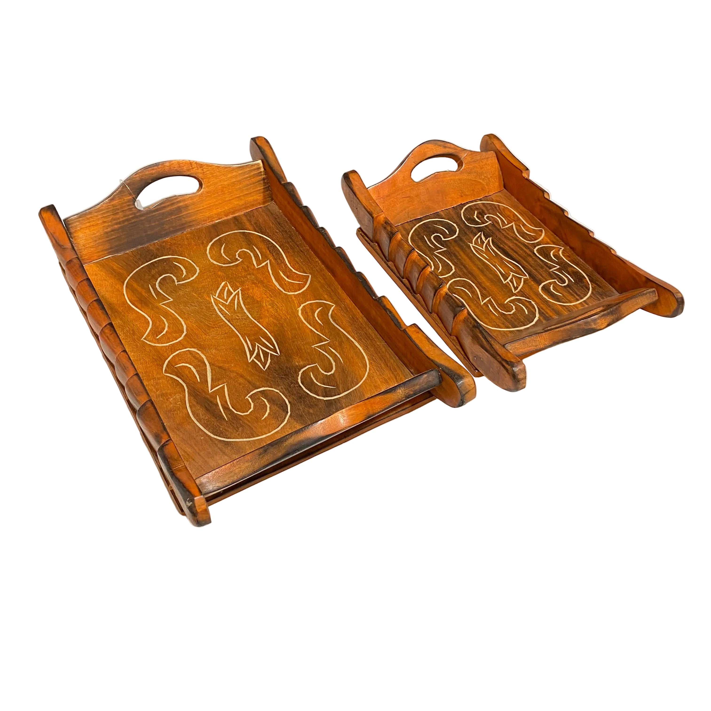 Two carved wooden serving trays with handles, displayed on a white table in what appears to be a workshop or storage area.