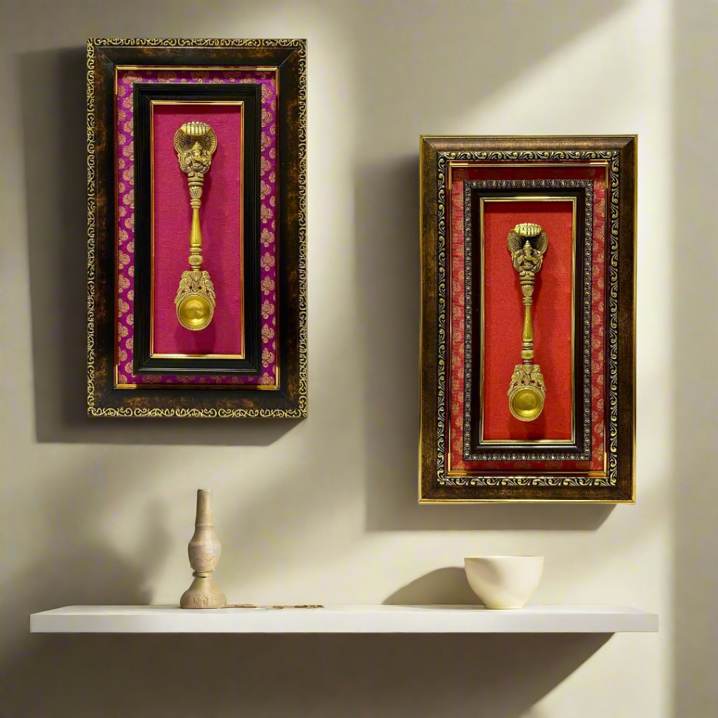 Two decorative wall hangings with gold spoons in ornate frames on a white background