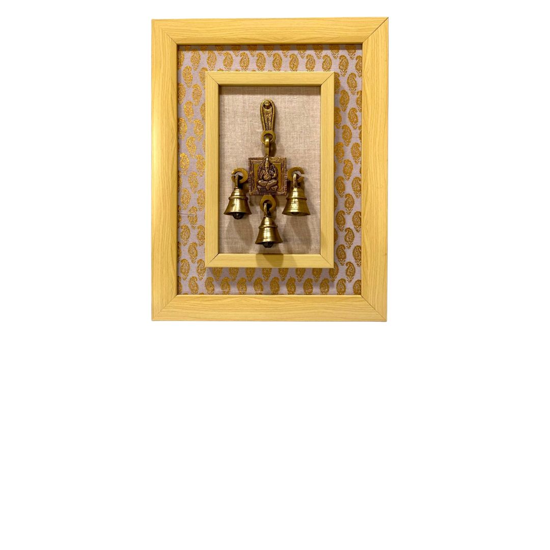 Decorative wall art with a gold frame and three small brass bells on a white background